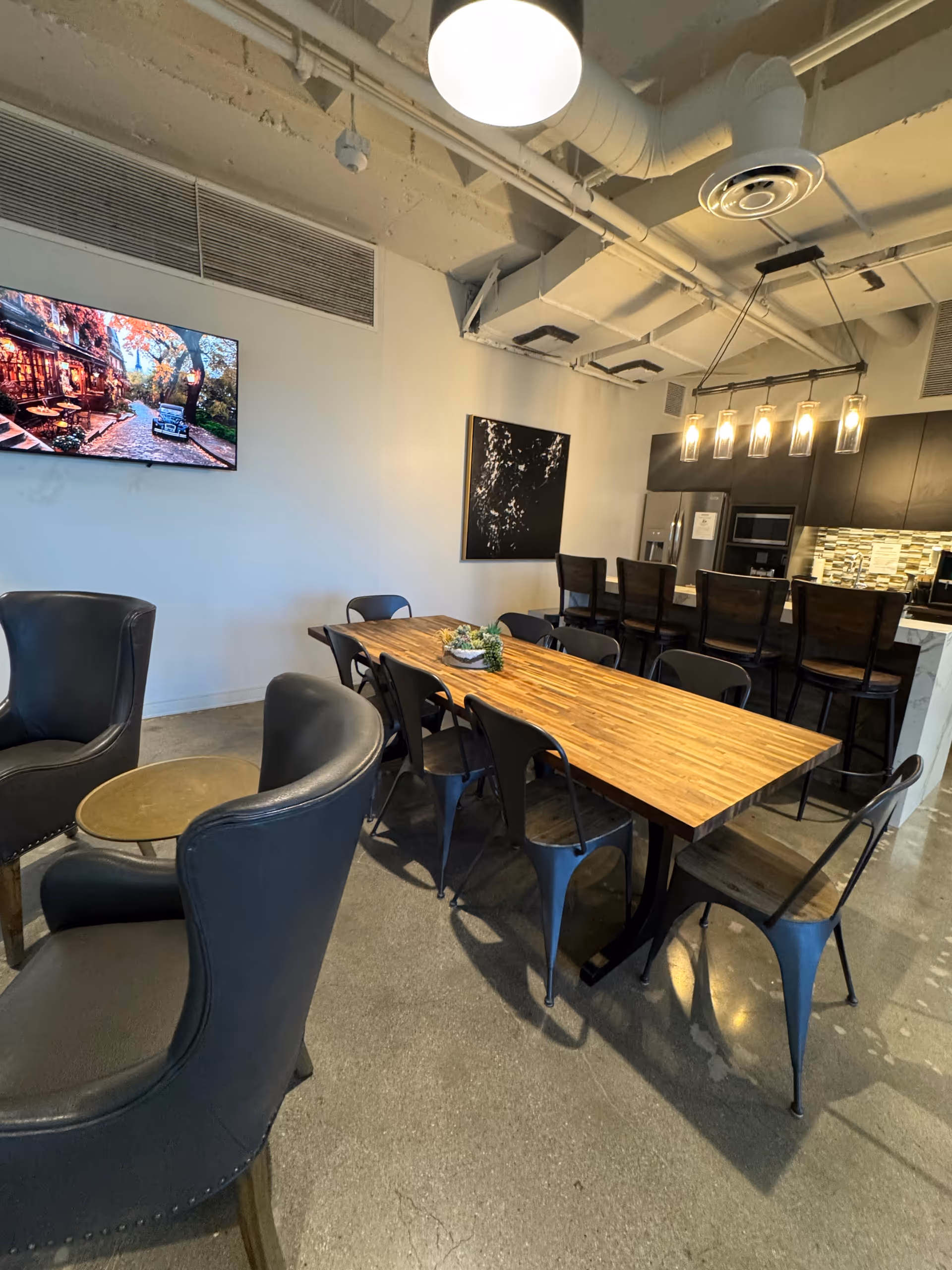 A modern dining area featuring a long wooden table, black chairs, and a kitchen bar.