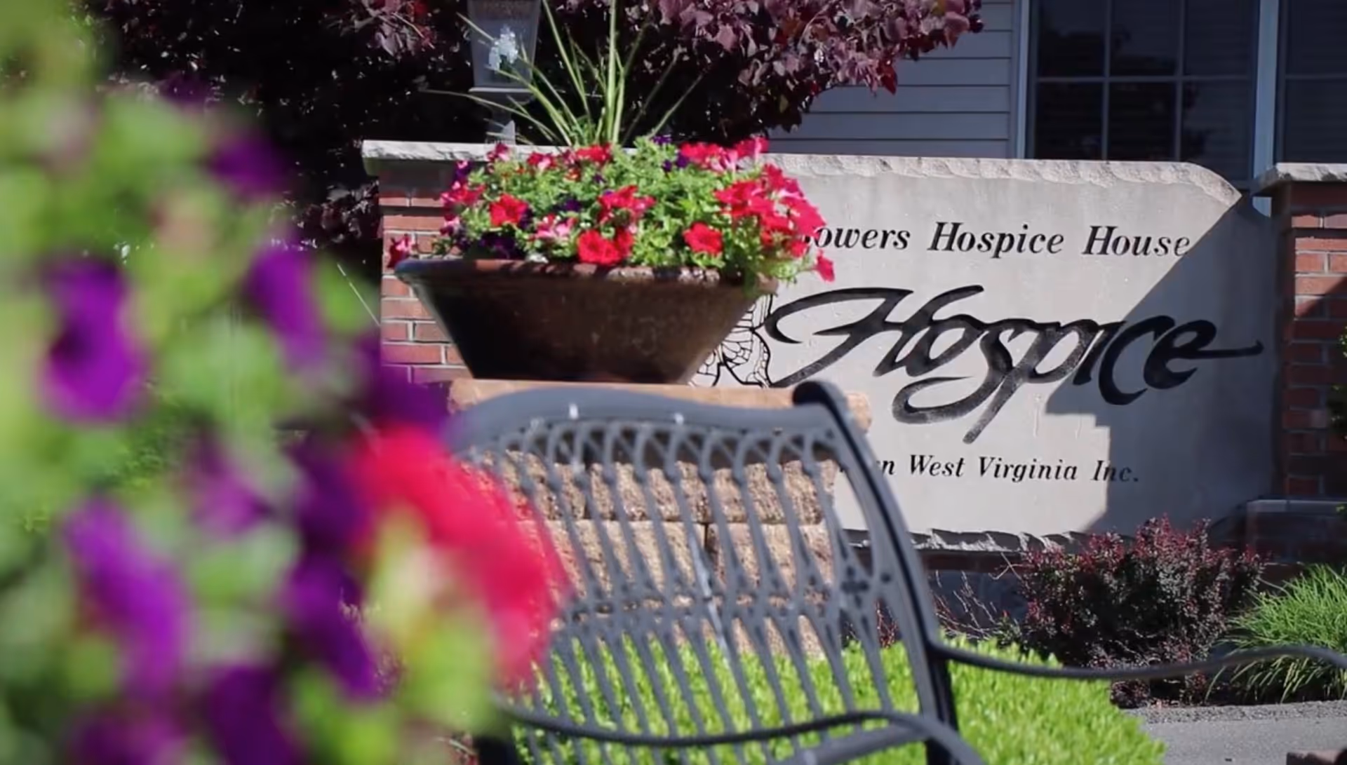 Outdoor scene with flower planters, a metal bench, and Hospice of Southern WV sign.