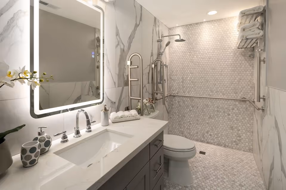 Modern marble bathroom featuring double sink, backlit mirror, and accessible shower with grab bars.
