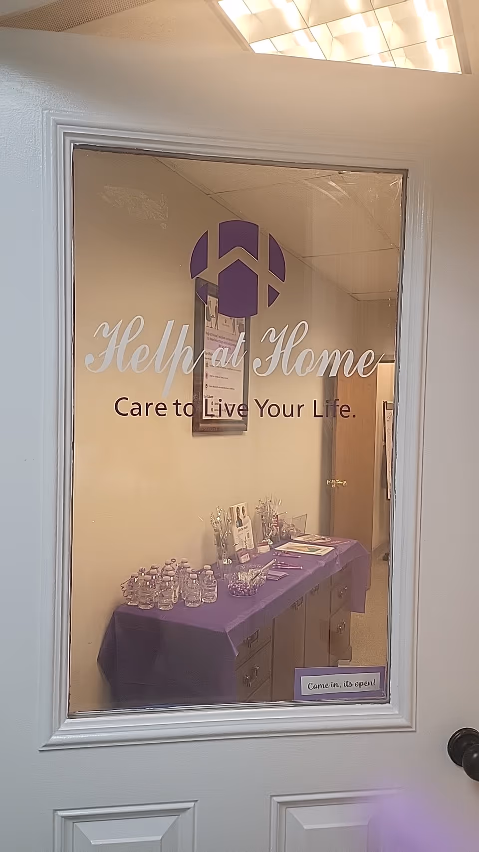 Interior doorway window reveals a purple-table setup with brochures and water bottles.