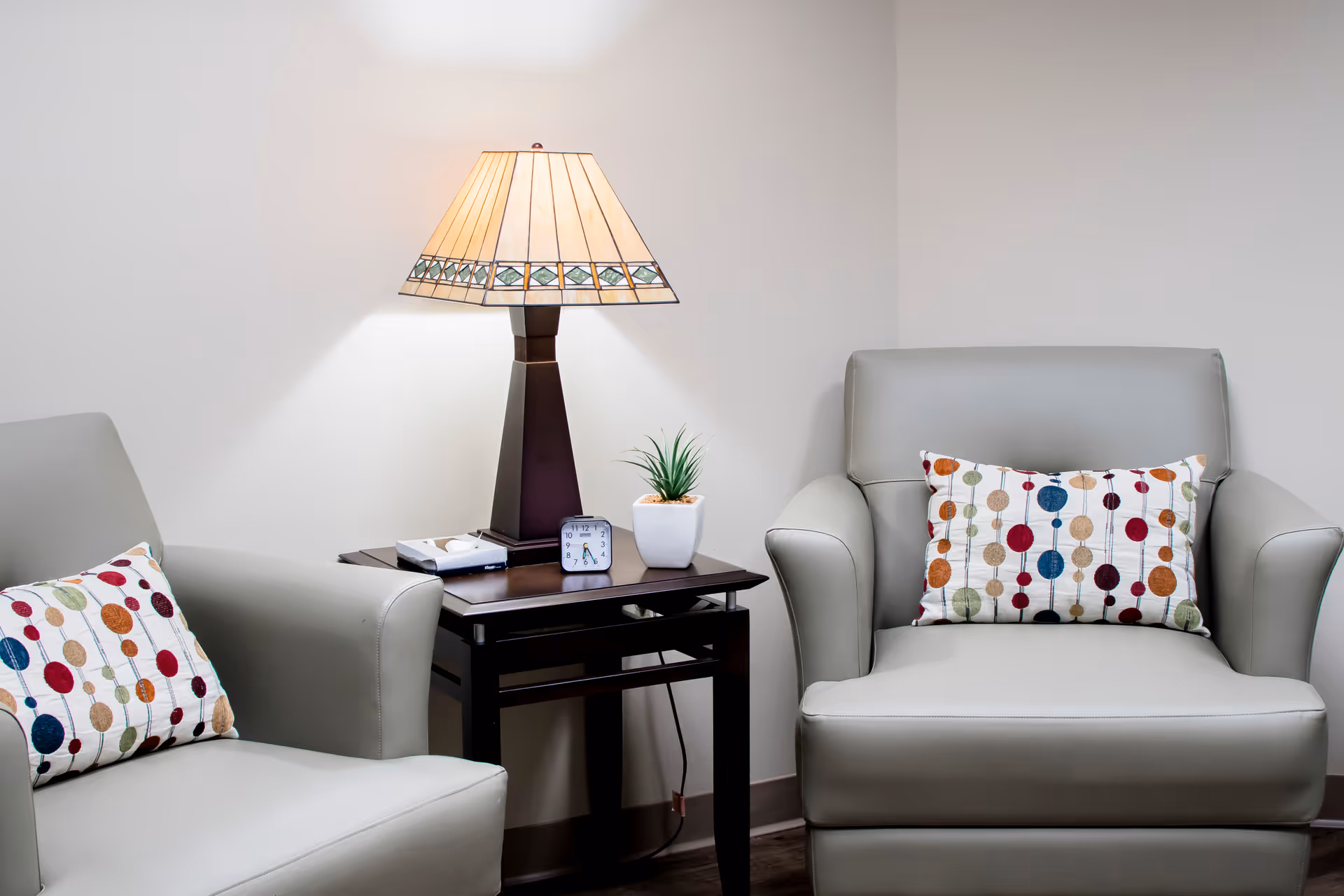 Two gray armchairs with cushions beside a side table and lamp.