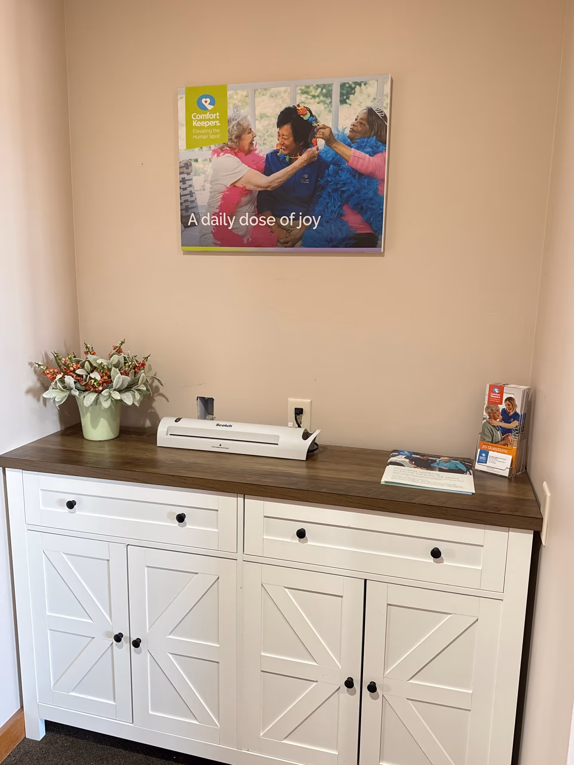 White cabinet with dark wood top, printer, brochure, and flower vase against beige wall.