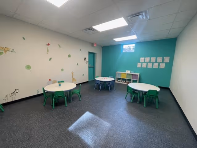 Bright therapy room with round tables, green chairs, and wall decals for children.