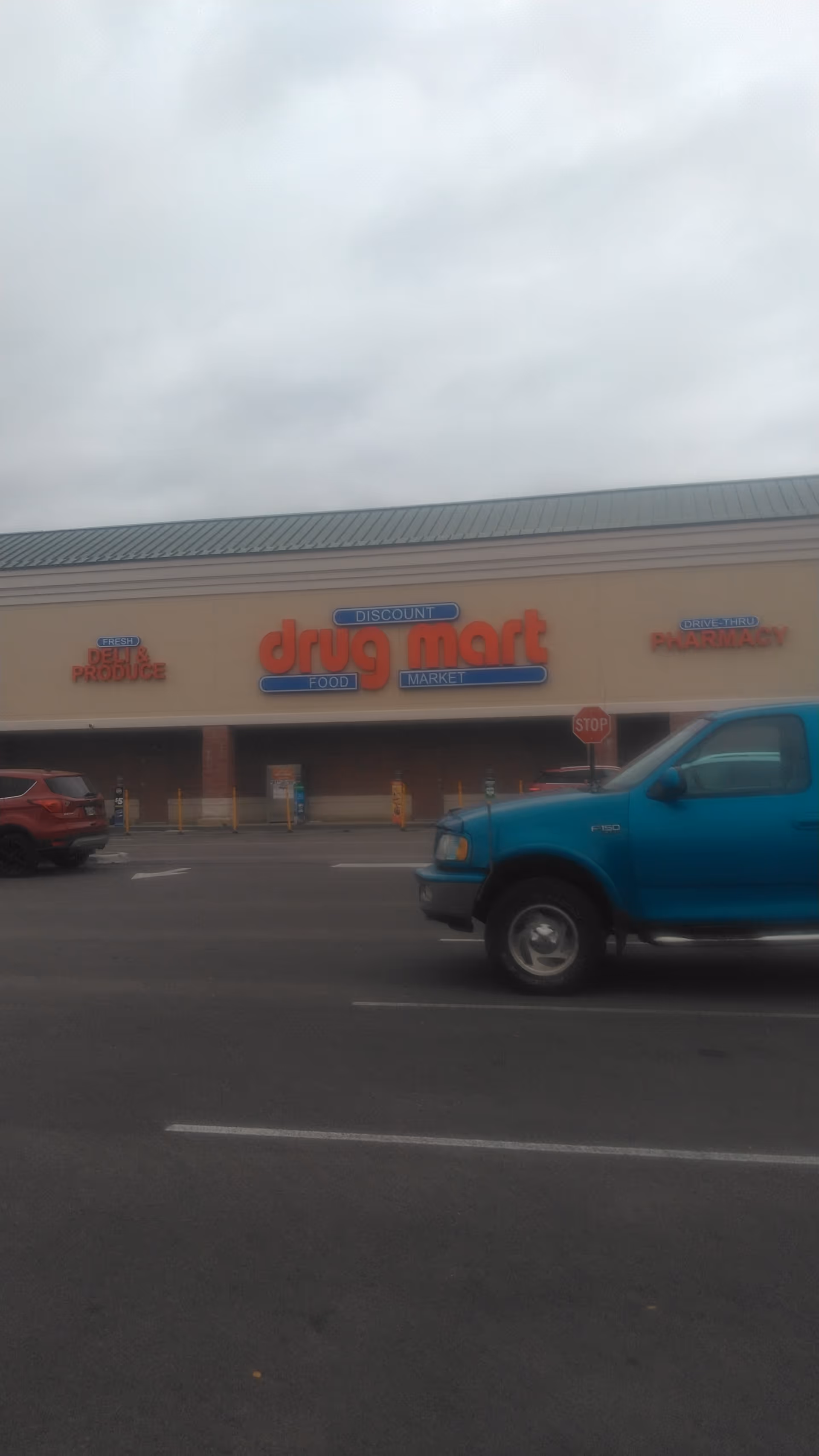 Blue pickup truck in parking lot in front of Discount Drug Mart storefront.