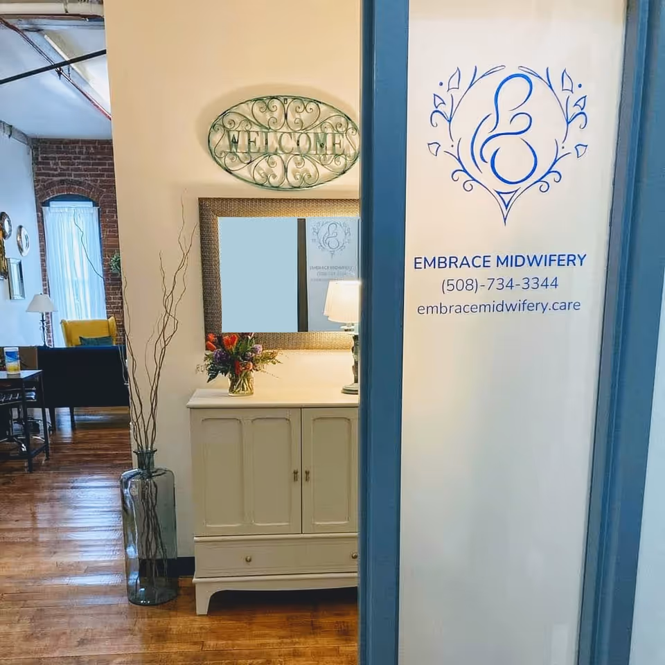 Interior reception foyer with a welcome sign, mirror, flowers, and Embrace Midwifery branding.