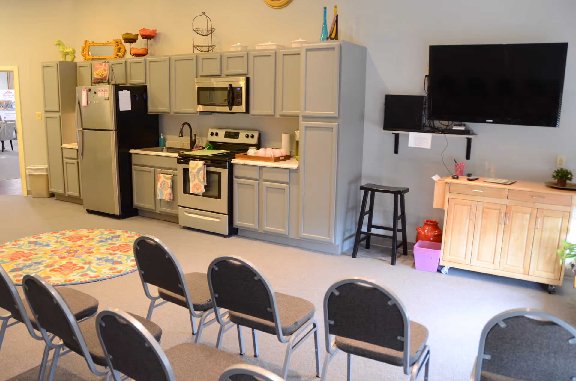 Common living area with kitchen appliances, folding chairs, a TV, and a wooden cabinet.