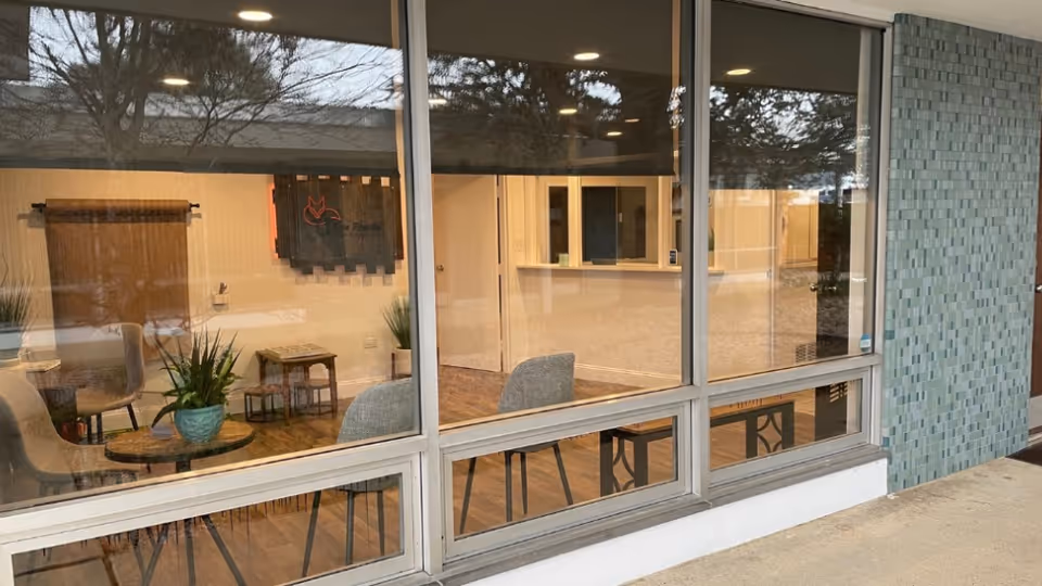 Interior waiting area visible through large glass windows with chairs, tables, and plants.