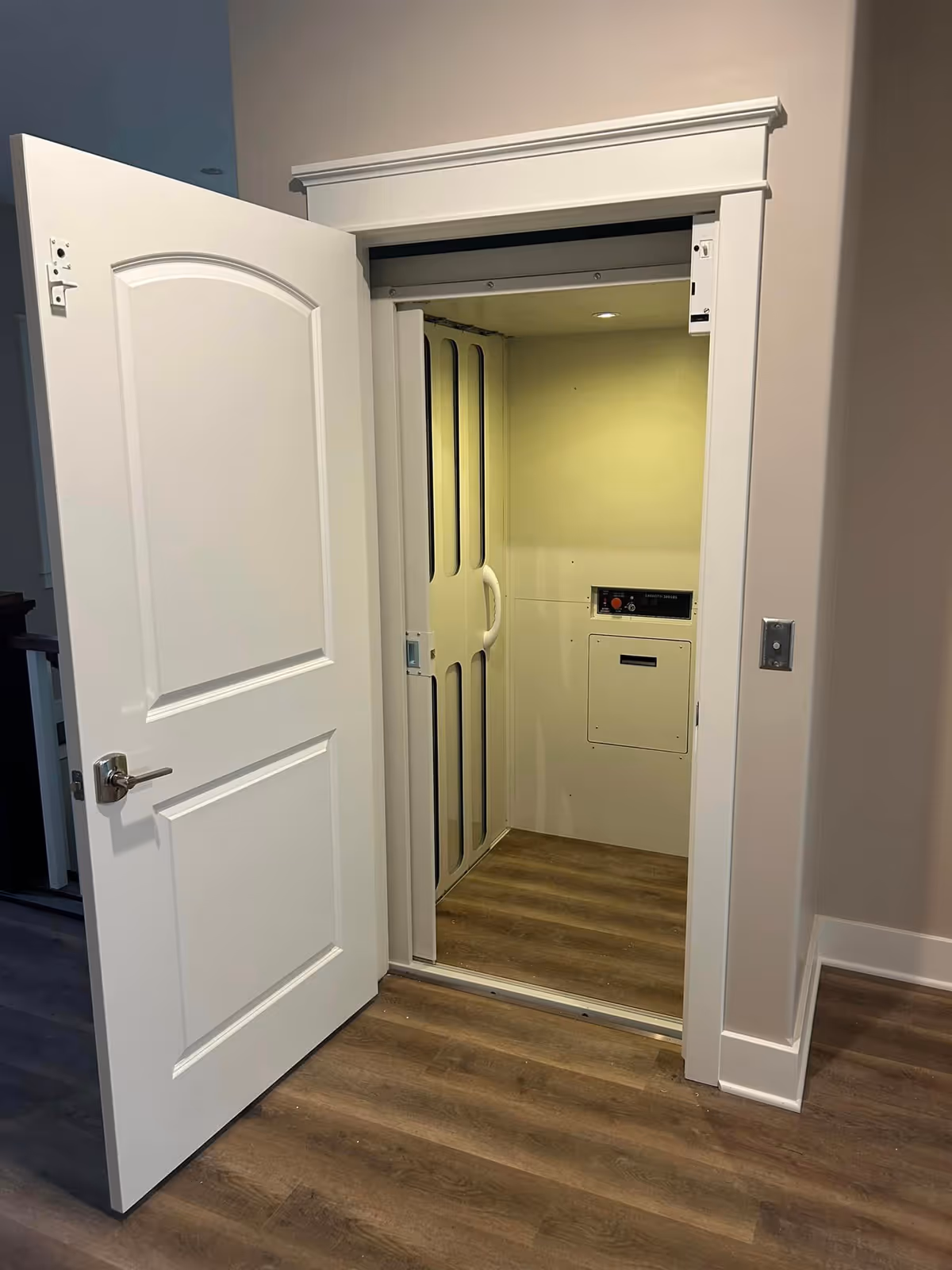 White interior elevator with open door, showing cabin and wood-look flooring.