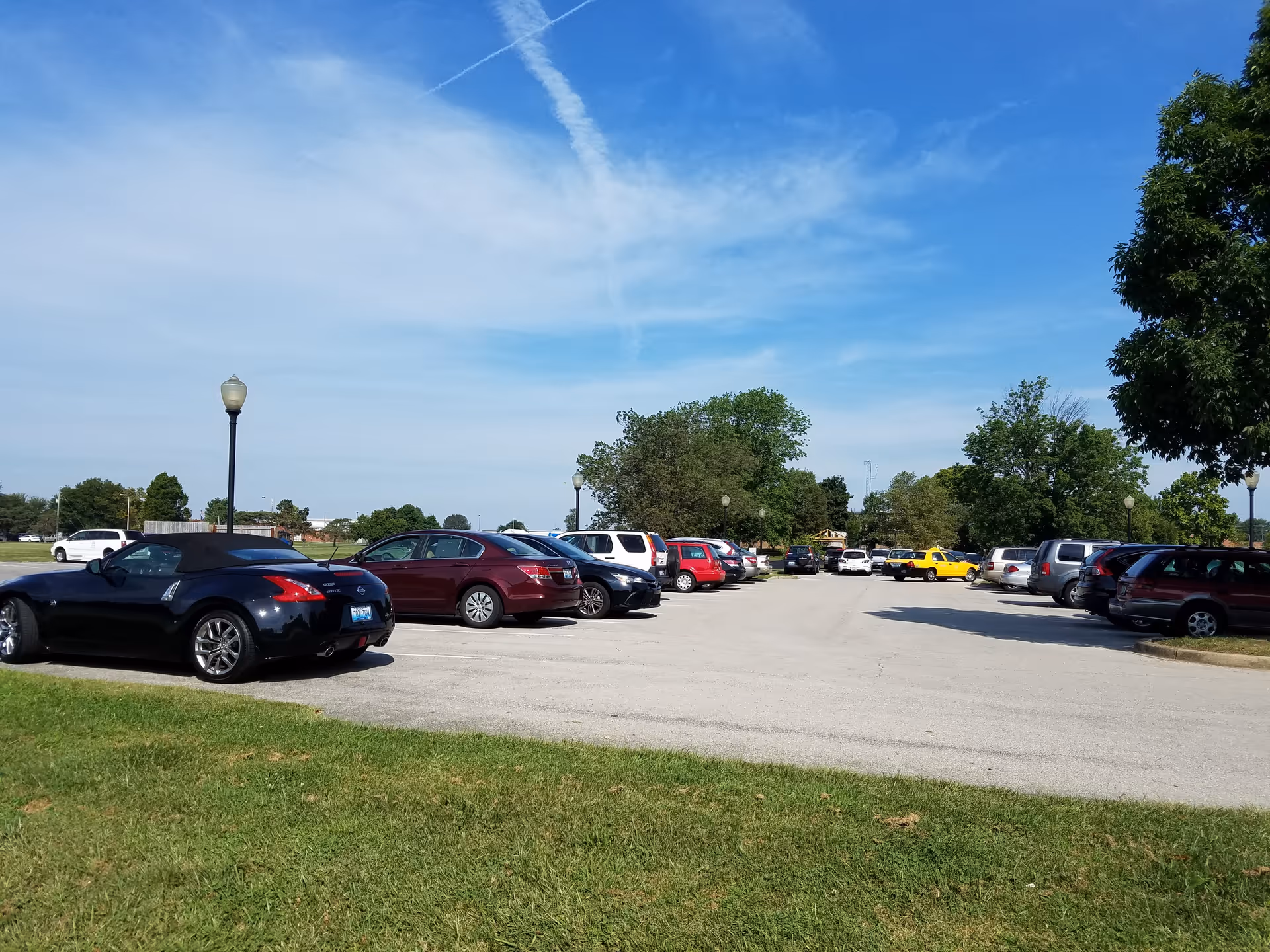 Sunny parking lot with many cars and green trees under a blue sky.