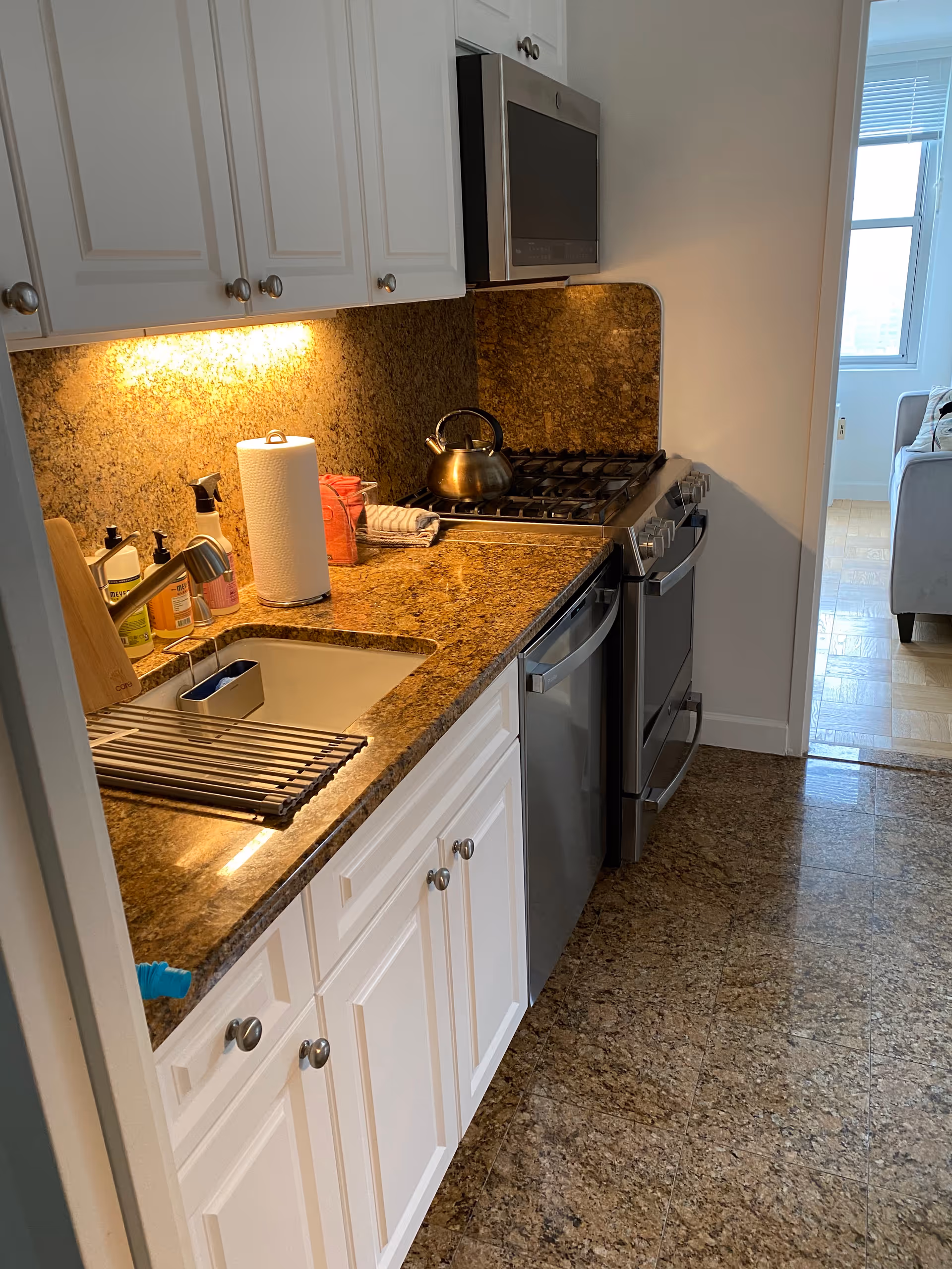 White kitchen with granite countertops, sink, stove, microwave, and under-cabinet lighting.