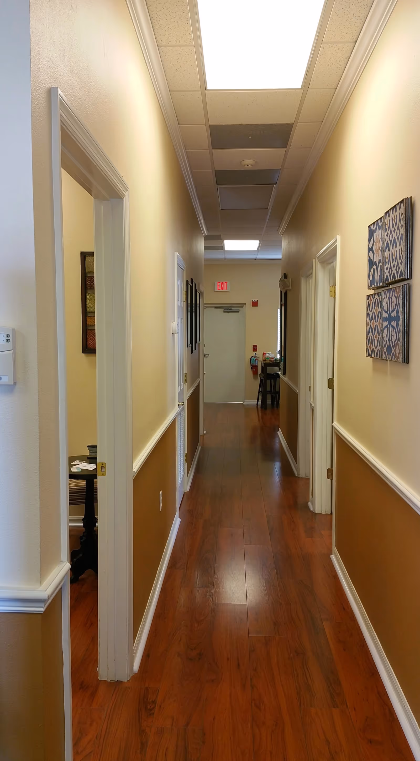 Long, well-lit hallway in a senior living facility with doors and artwork.