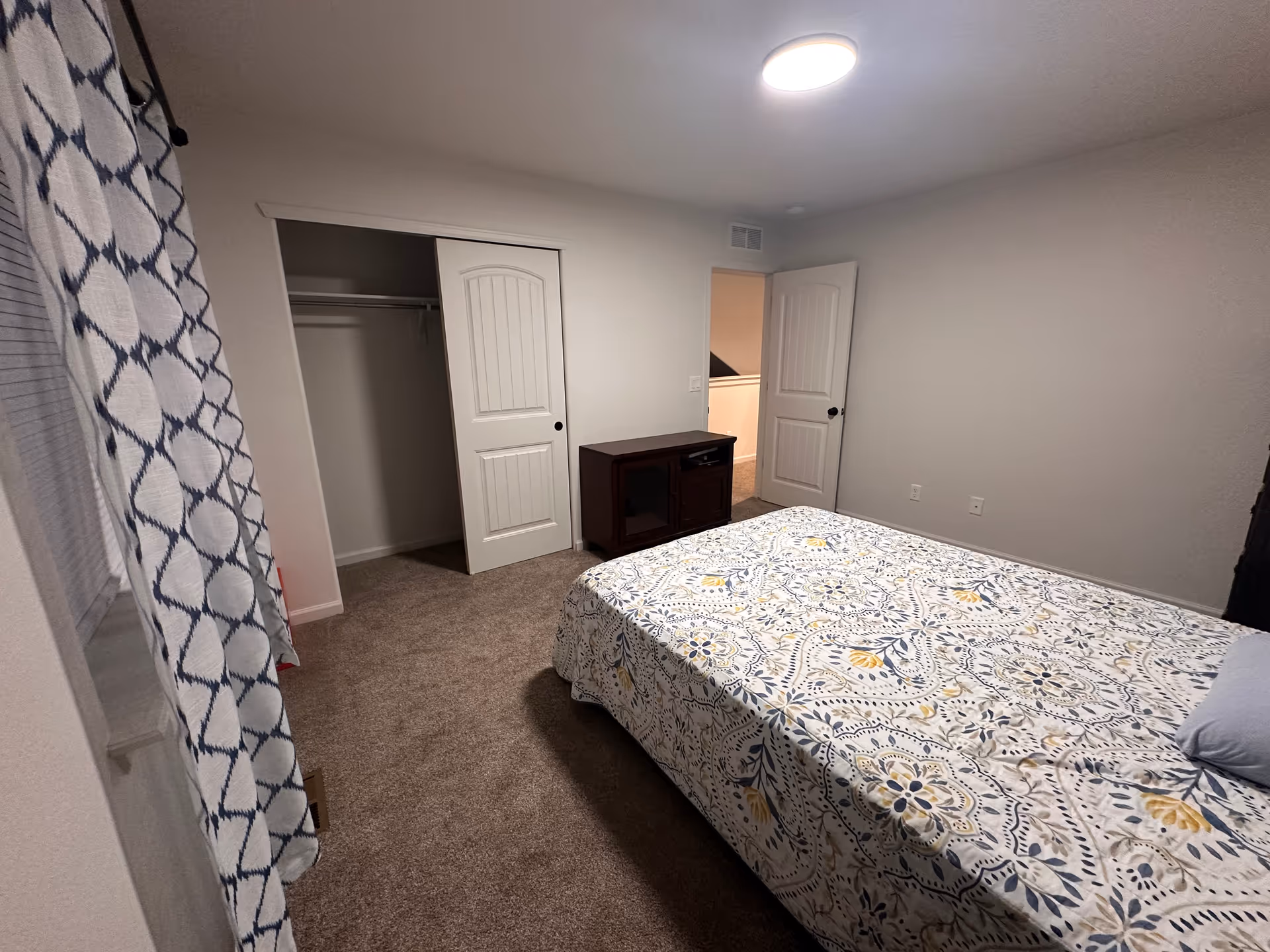 A furnished bedroom with a bed, closet, dresser, and patterned bedspread.