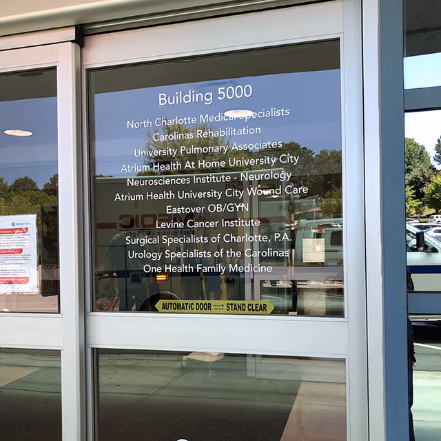 Glass entrance door showing Building 5000 and facility affiliations, with reflections of parked cars.