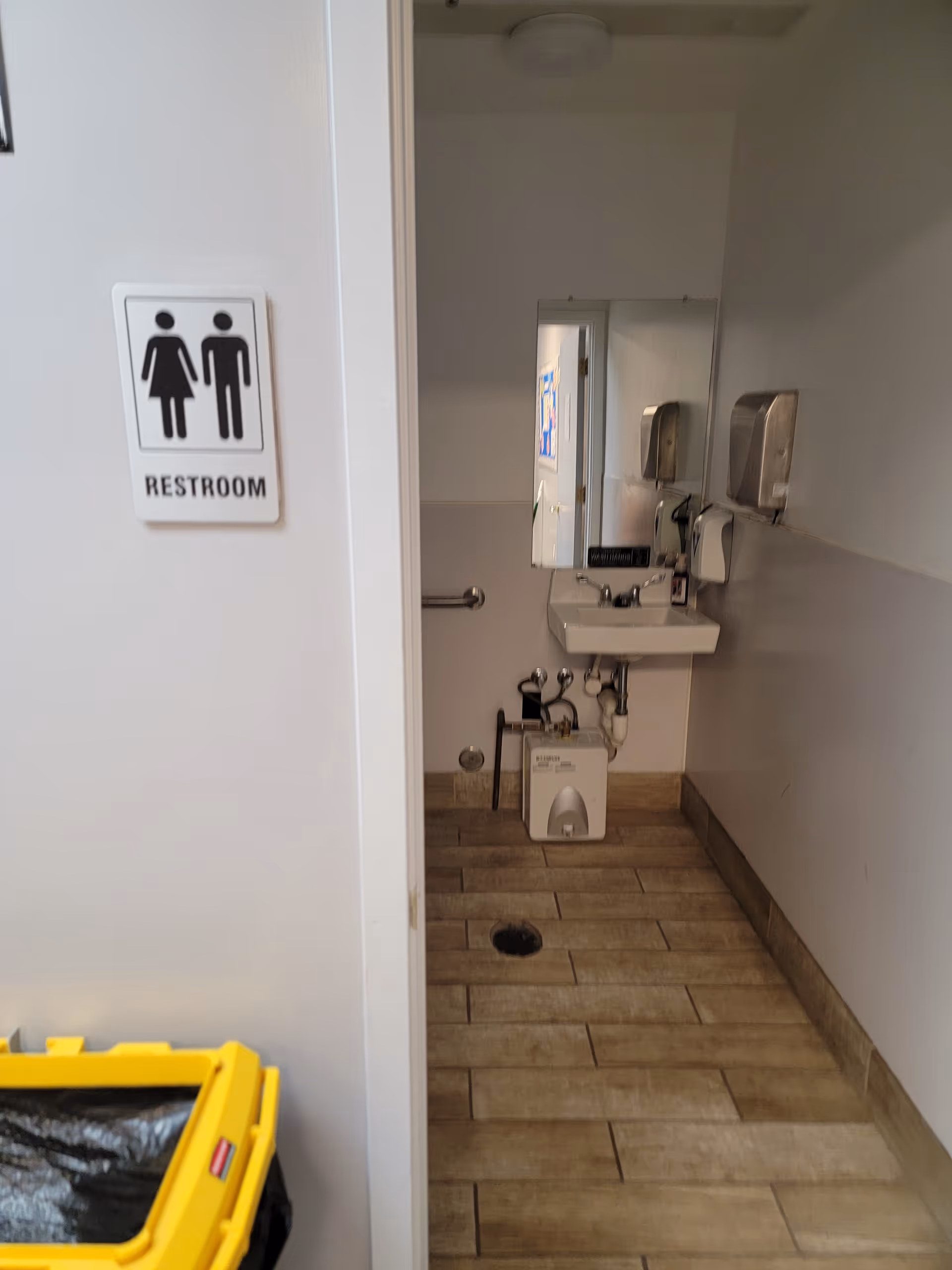 Doorway to a restroom with sink, mirror, soap, and paper towel dispensers.