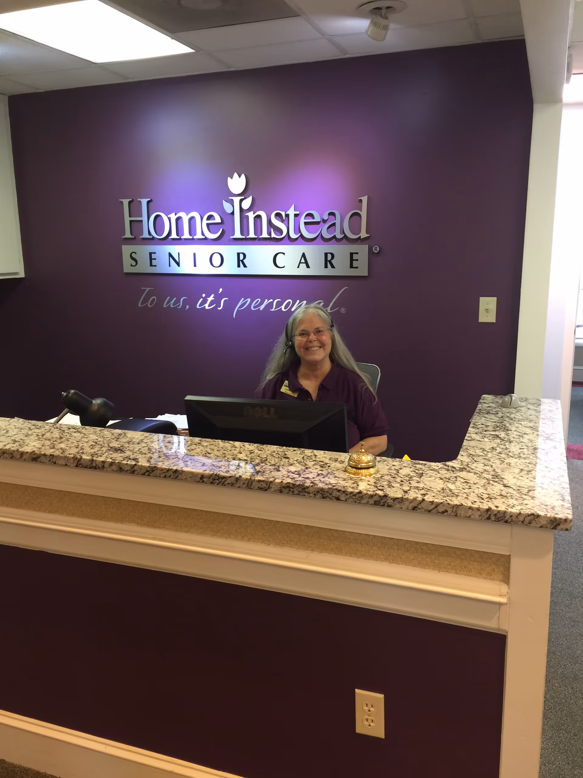 Receptionist at marble-front desk in Home Instead Senior Care lobby.