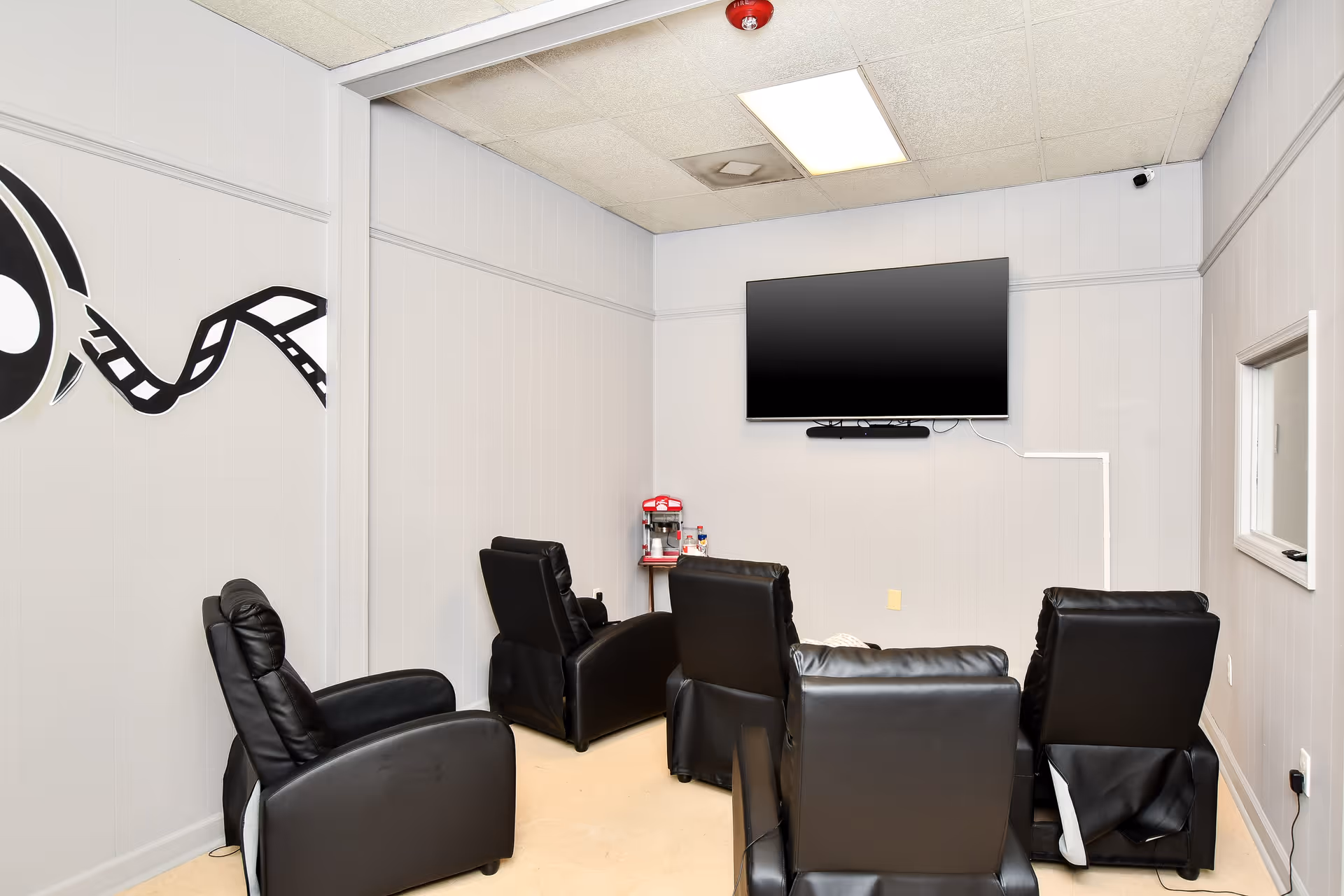 Small lounge area with black leather recliners, a wall-mounted TV, and a coffee station.