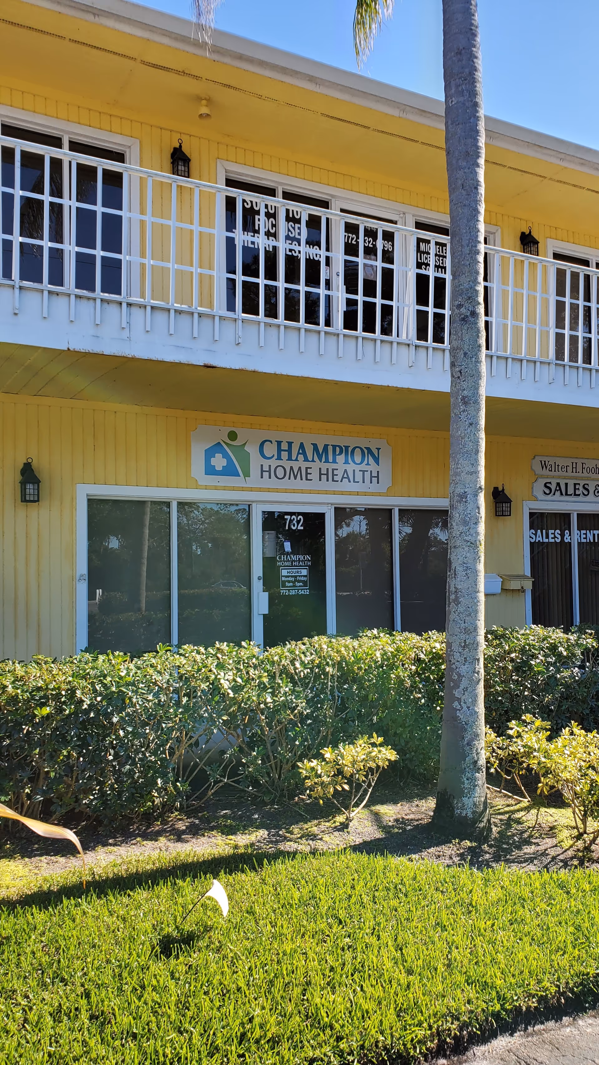 Yellow two-story building with a white railing, Champion Home Health sign, and palm tree.