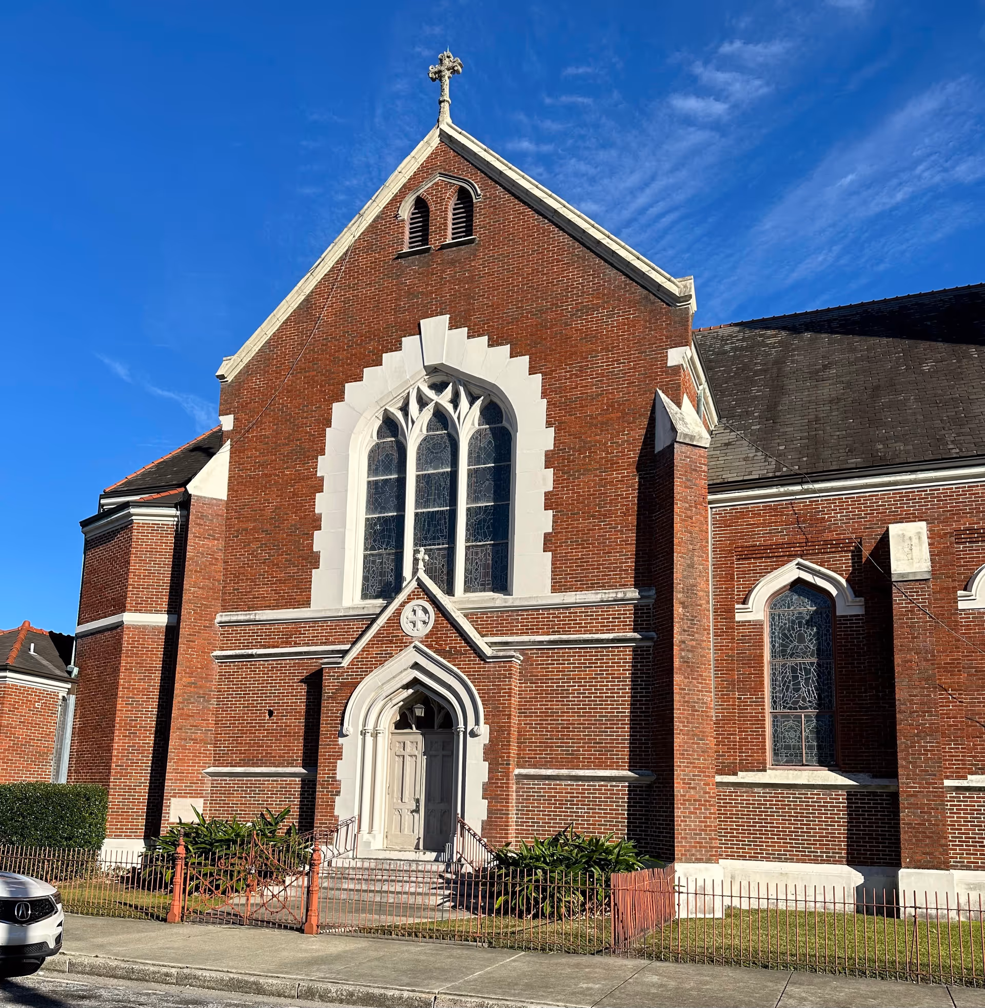 Brick church-style building exterior with a large arched window and cross against blue sky.
