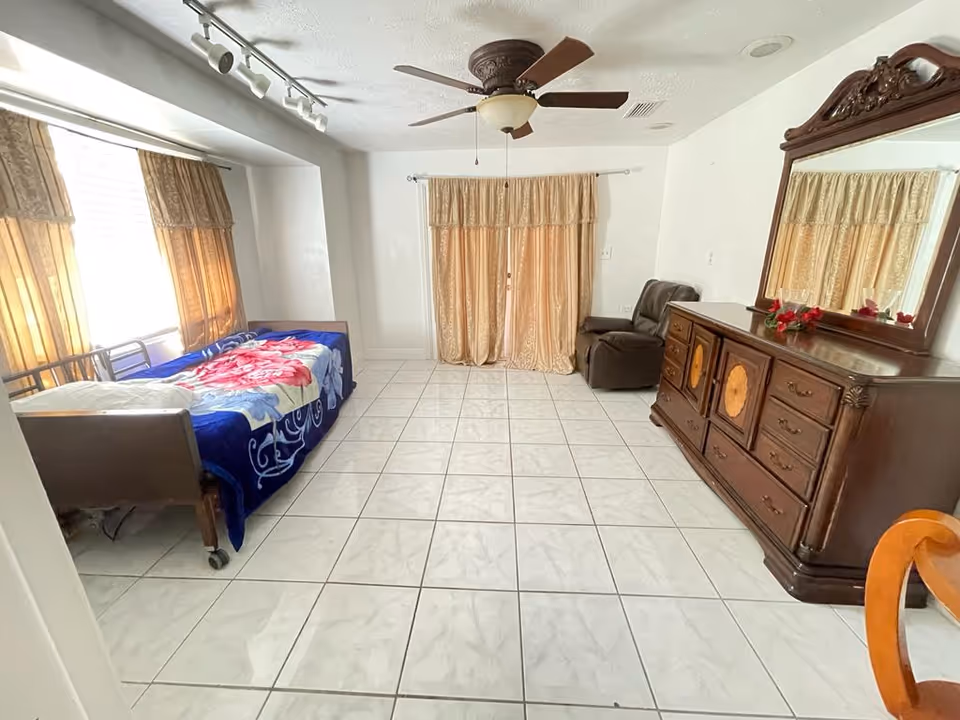 Furnished bedroom with a bed, dresser, and curtained windows.