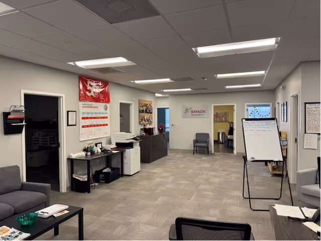 Reception area of BAYADA Pediatrics featuring chairs, desks, posters, a whiteboard, and a hallway.