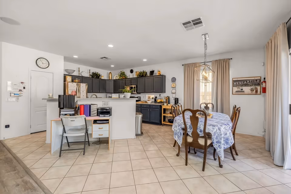 Bright open kitchen and dining area with dark cabinets, round table, and tile floor.