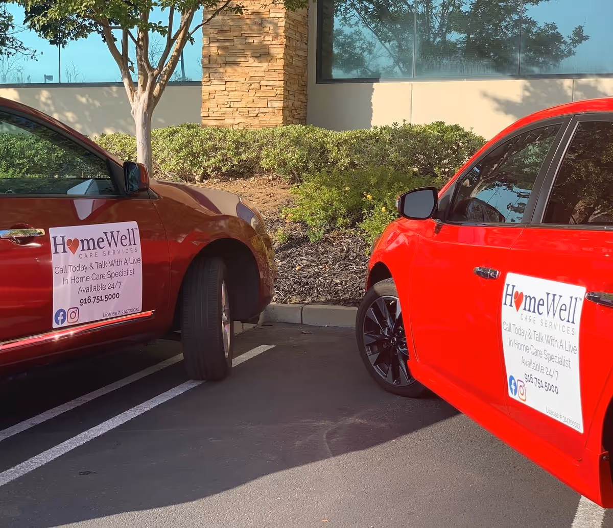 Two red HomeWell Care Services vehicles parked in a lot beside a modern glass-front building.