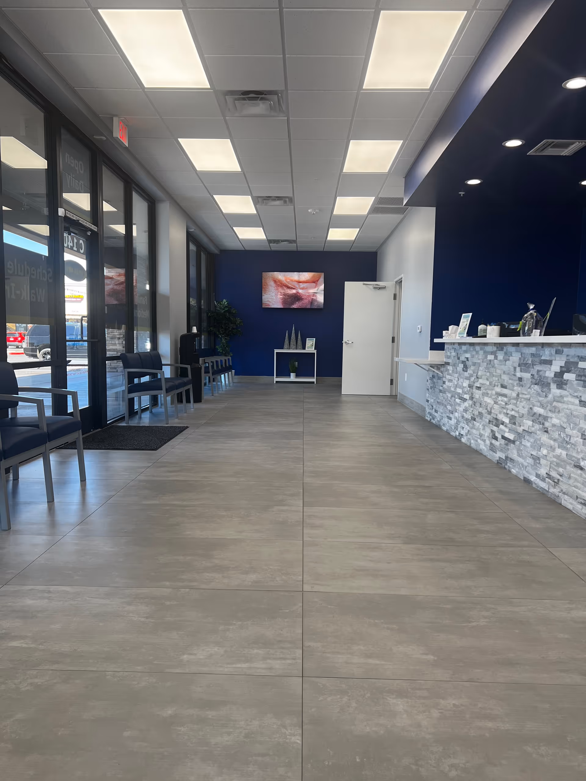Wide modern lobby with blue accent wall, stone reception desk, and seating along windows.