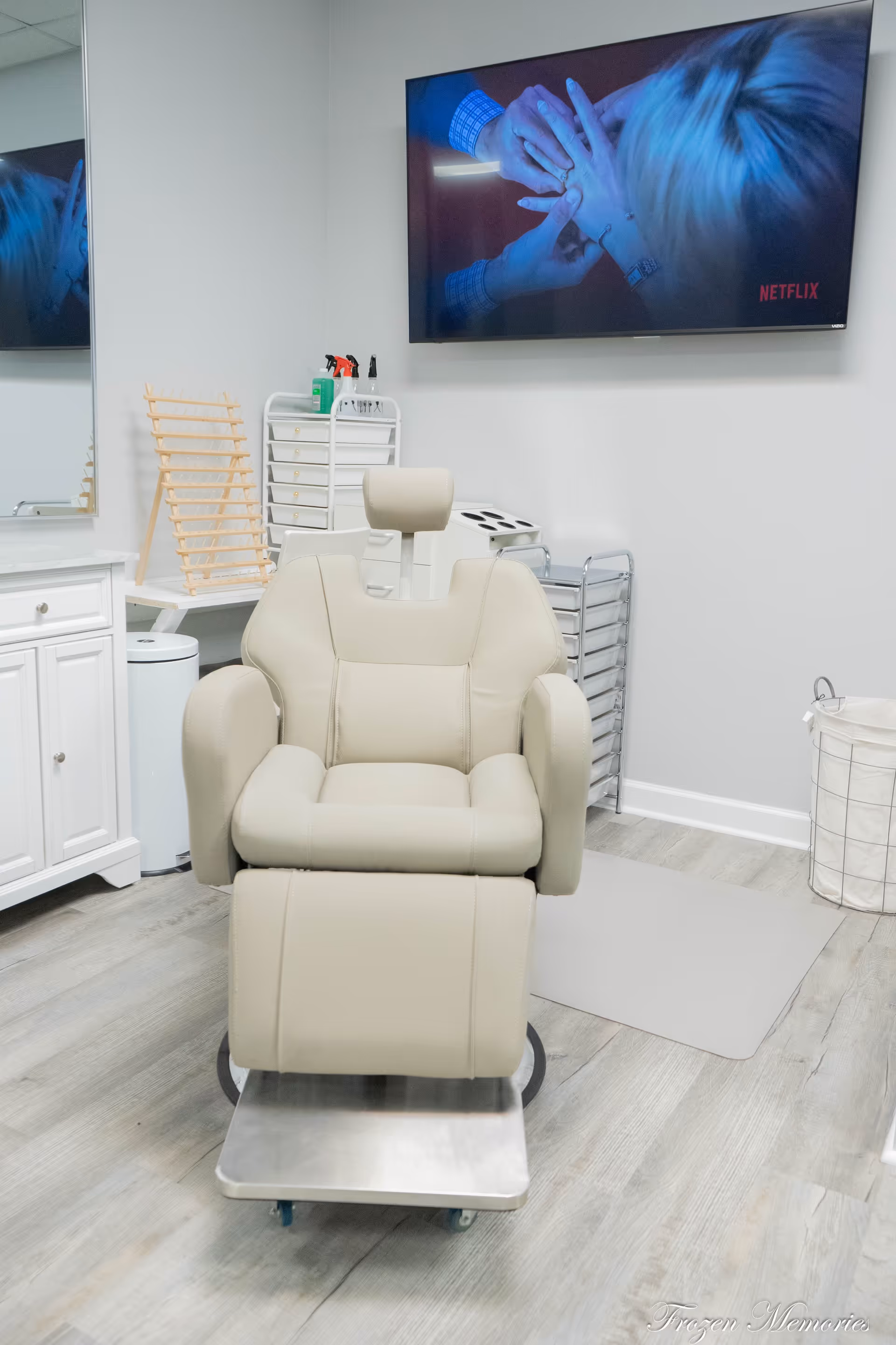Beige reclining chair on a wheeled metal platform in a bright clinic room with a TV