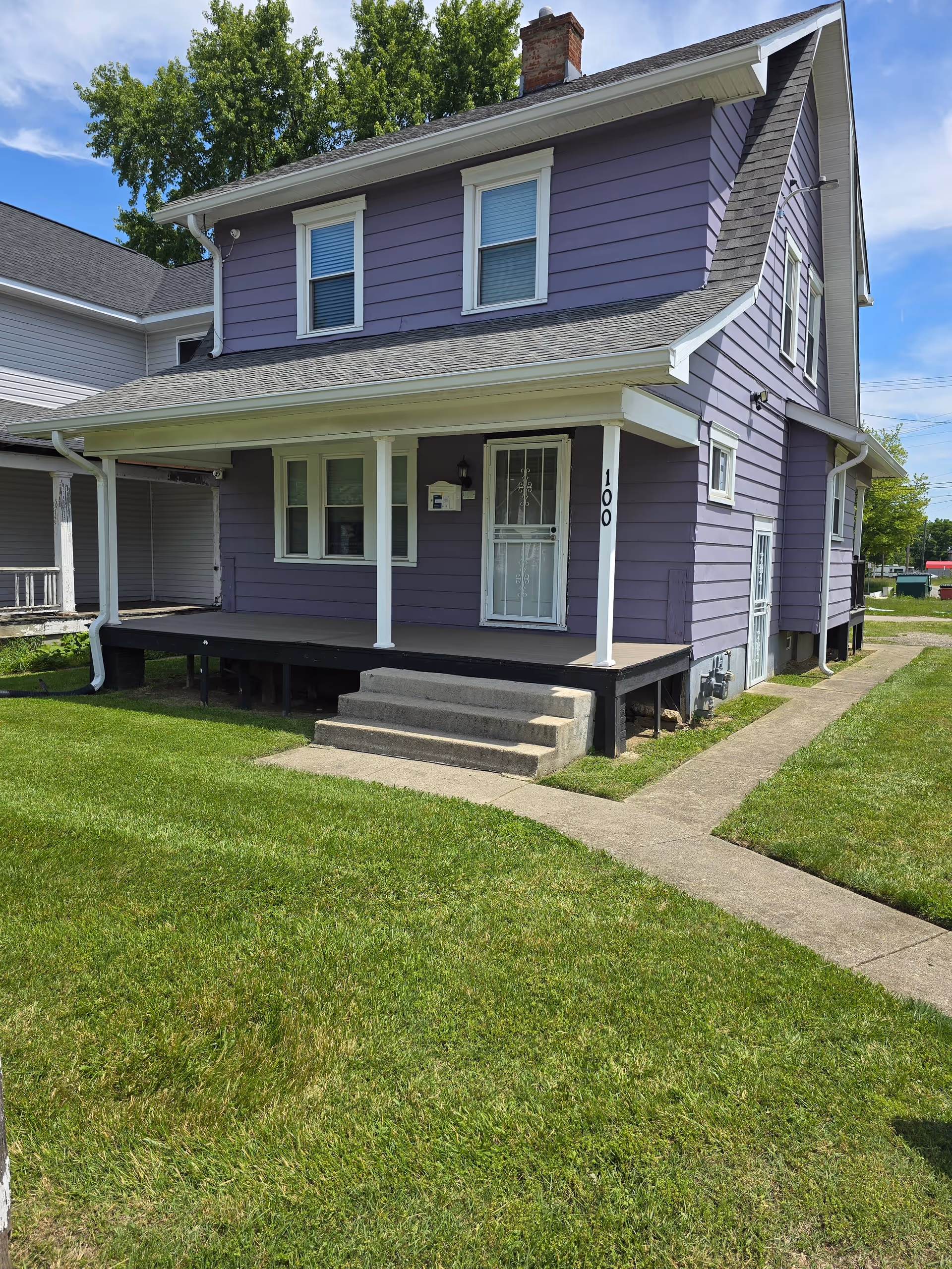Two-story purple house with a front porch, stairs, and green lawn.