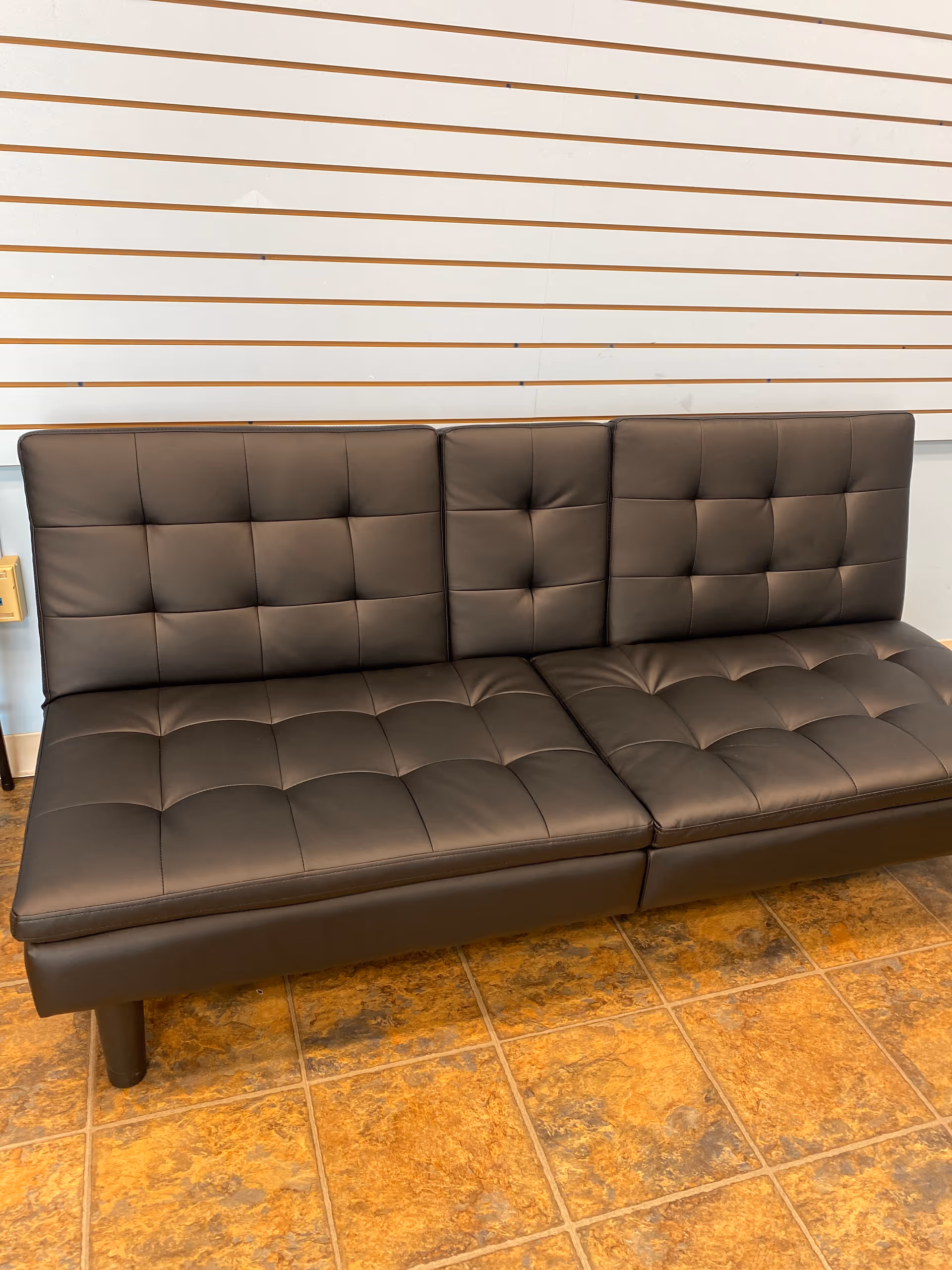 Brown tufted leather sofa against a striped wall in a tiled interior.