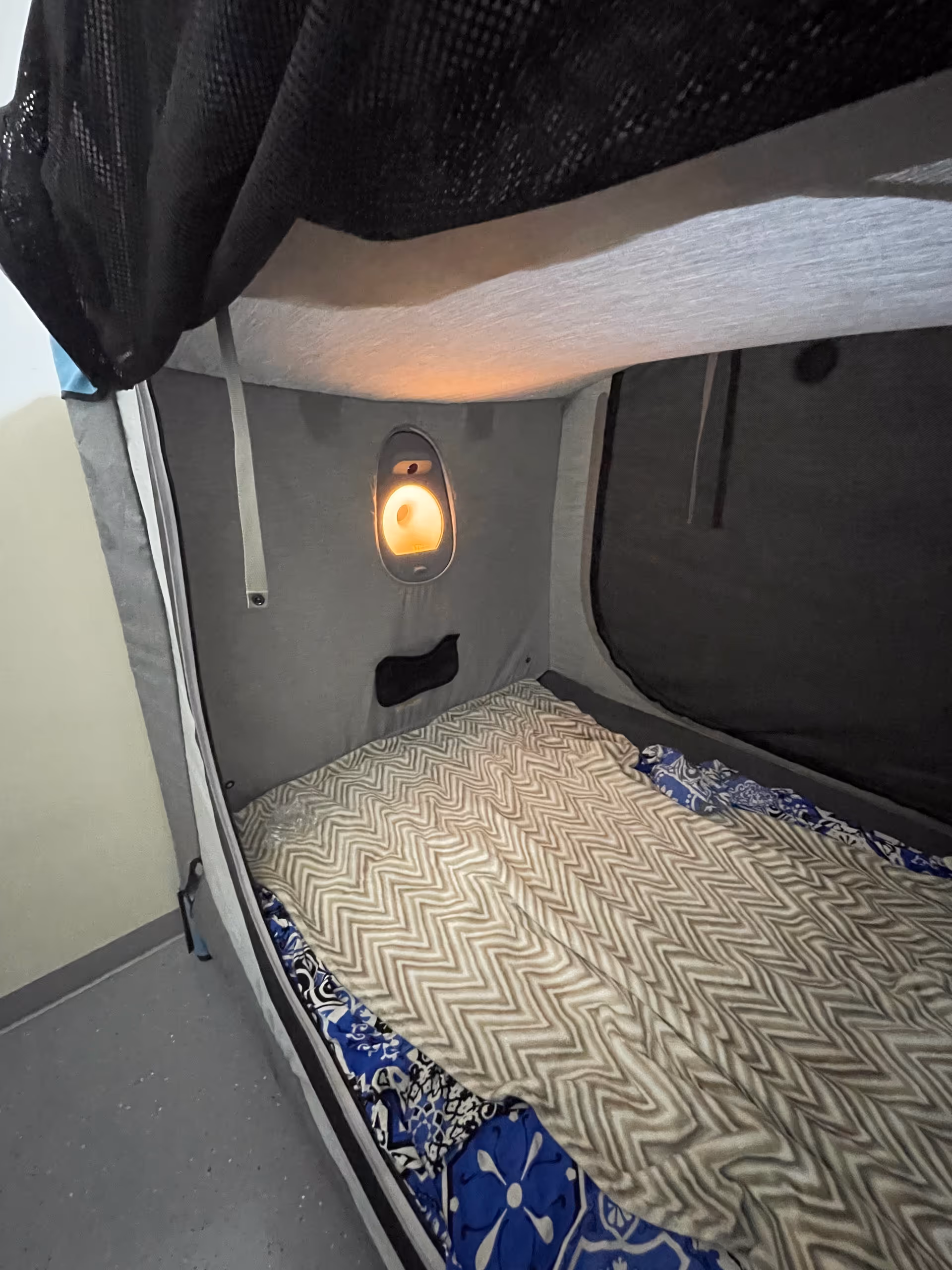 A compact private bed pod with a chevron blanket and warm light.