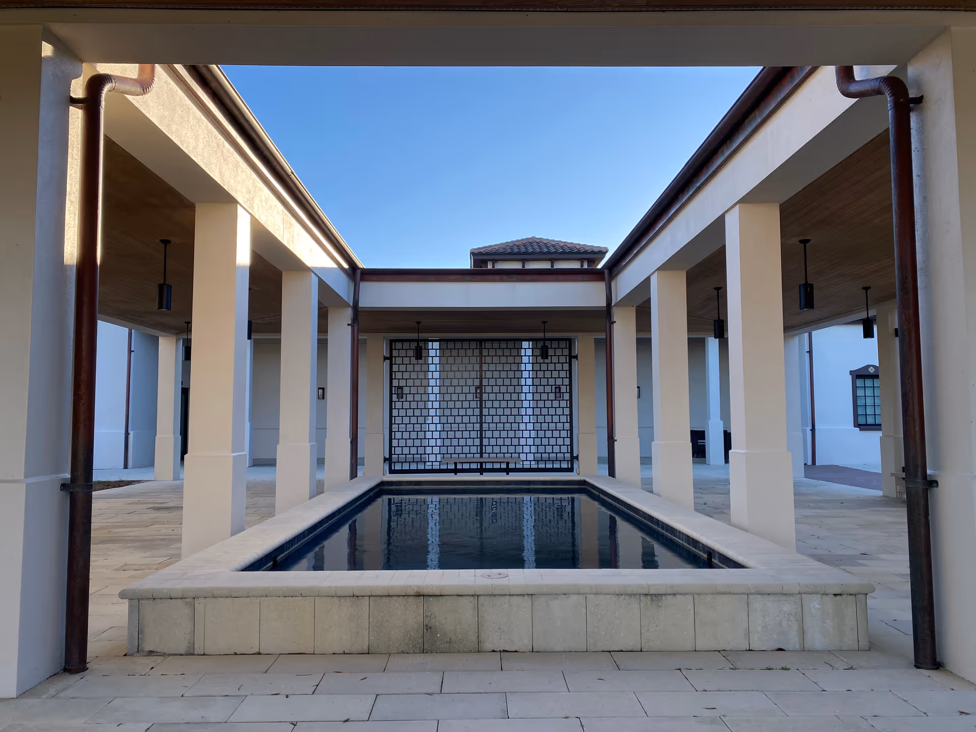 Open air courtyard with a central rectangular pool, white columns, and blue sky.