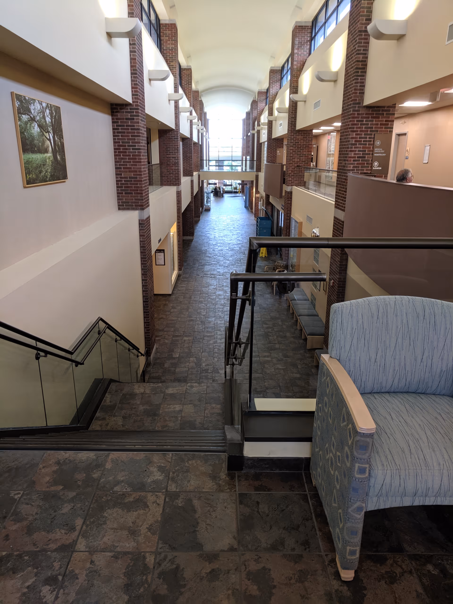 Bright multi-level atrium hallway with brick columns, railings, and seating.