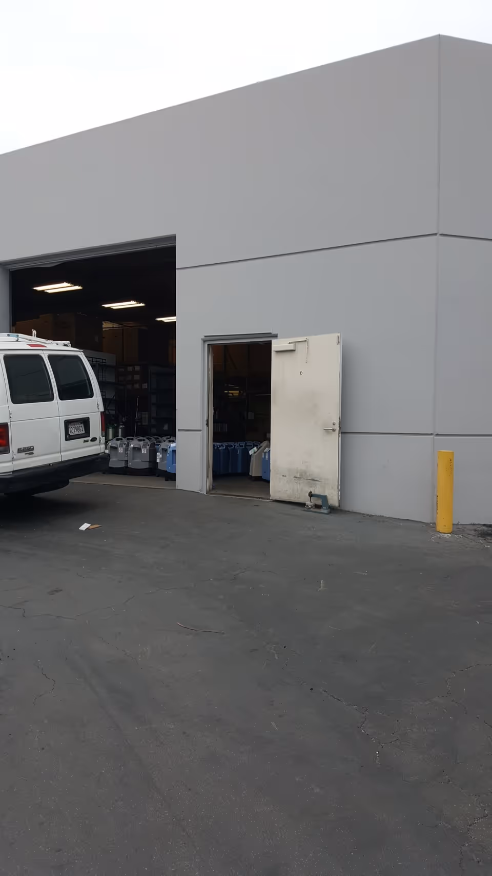 Exterior view of a large light-gray building with an open loading bay and a white van.