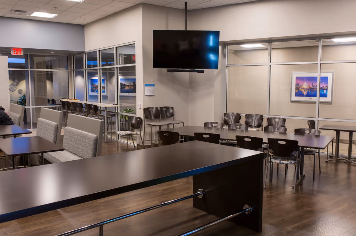A modern senior living facility dining area with tables, chairs, and a wall-mounted TV.