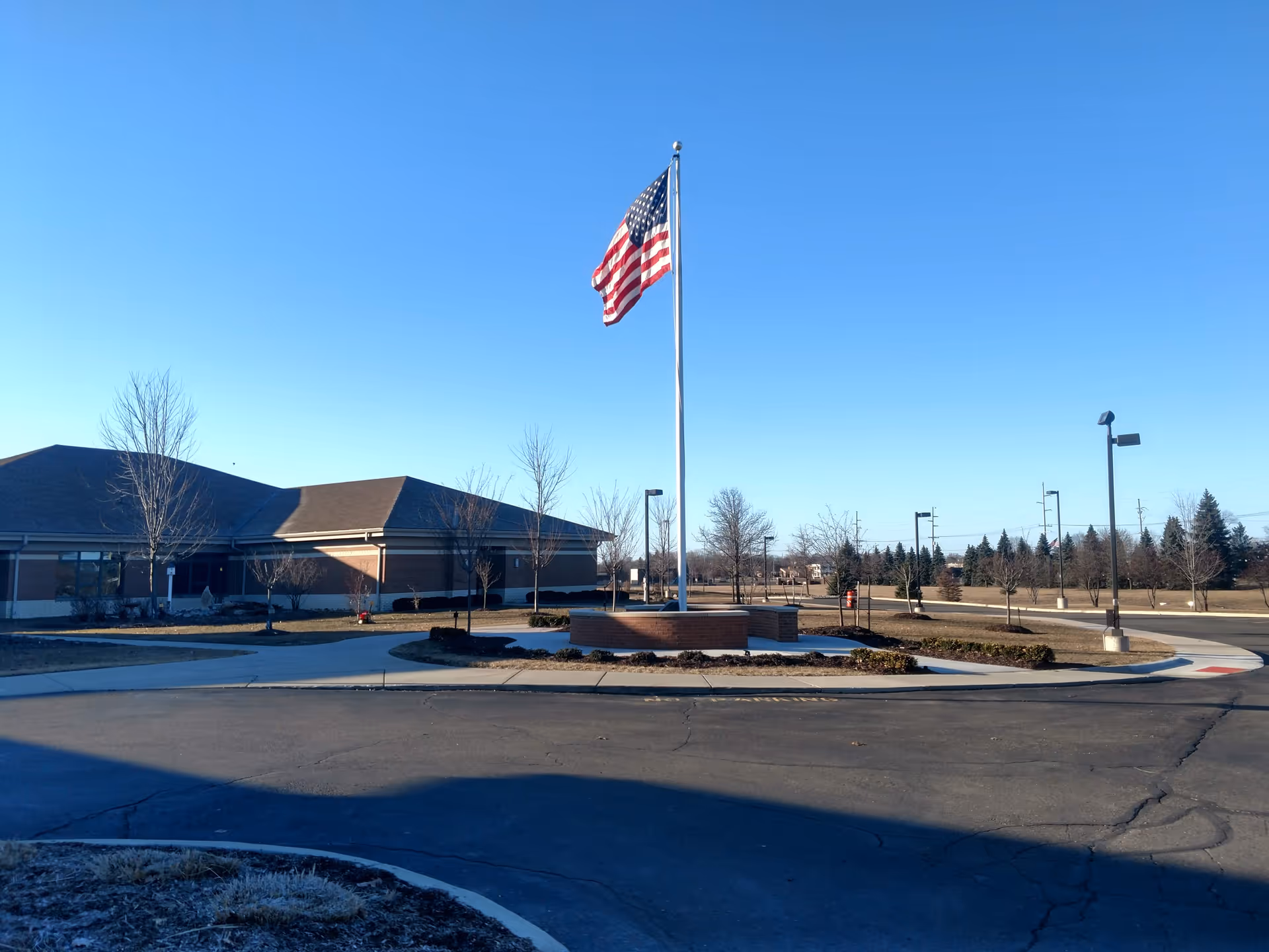 American flag on a tall pole in a circular driveway with a brick building behind.