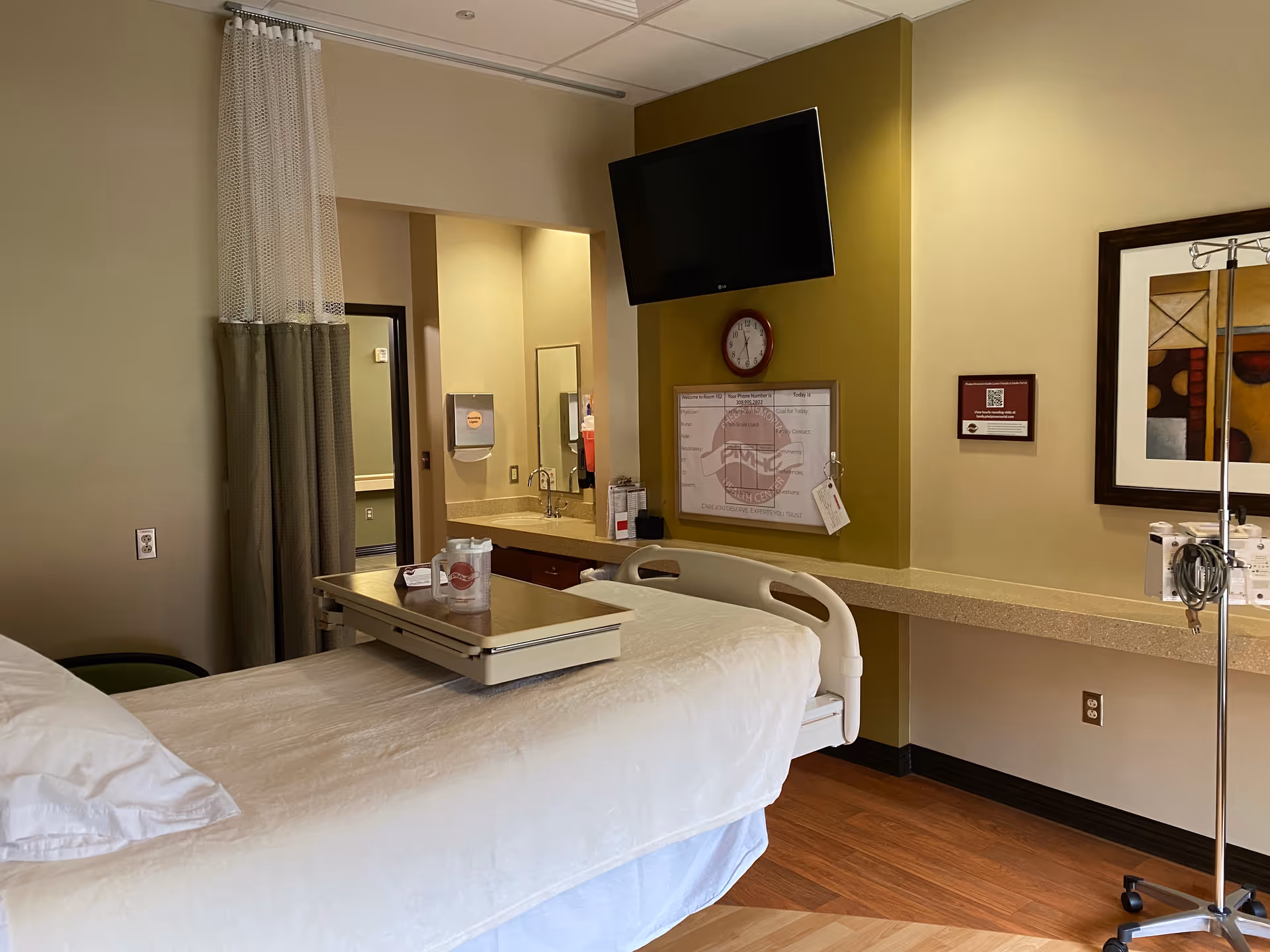 A patient room with a bed, curtains, TV, and medical equipment.