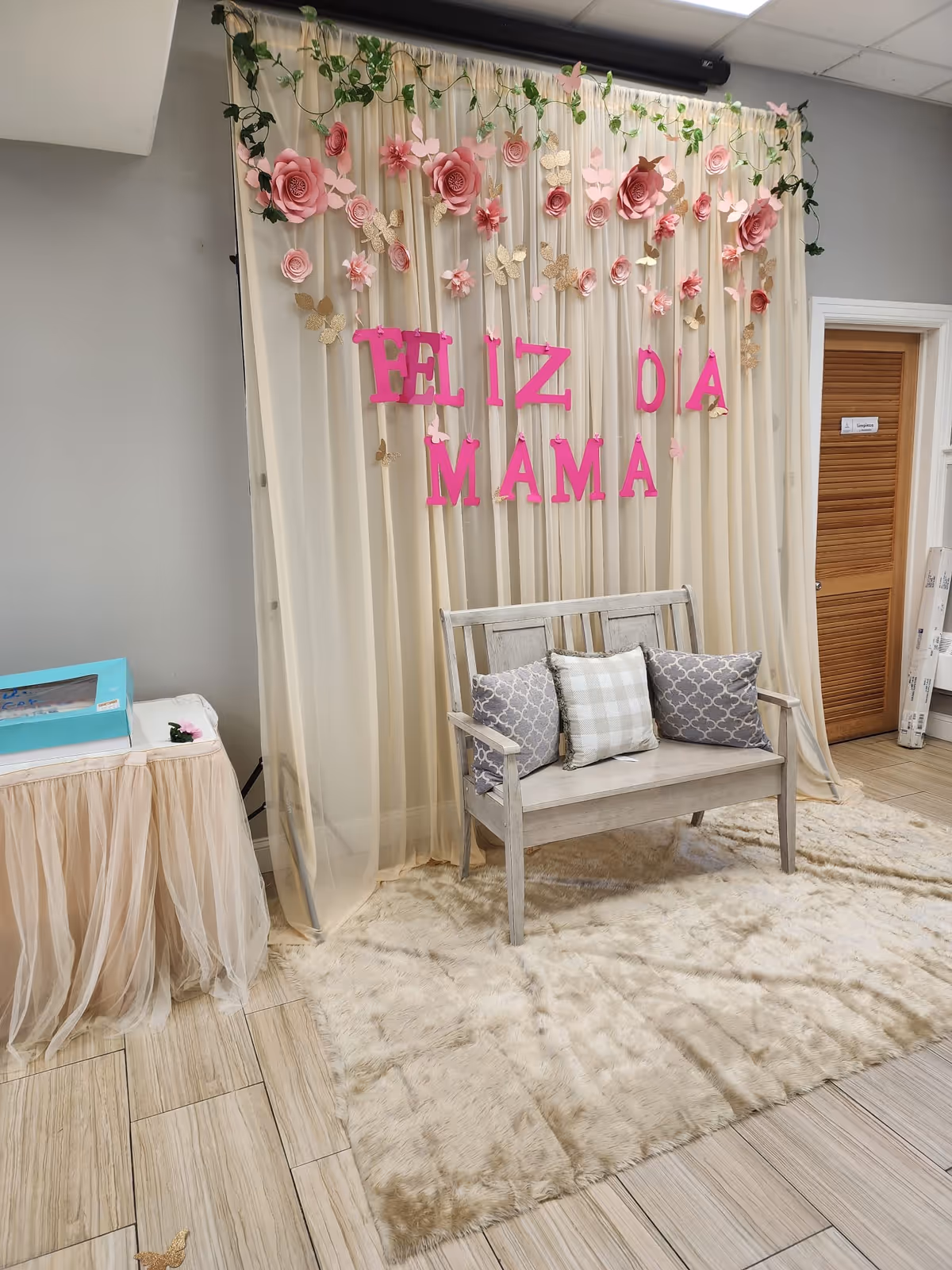 Cream draped backdrop with pink flowers and a wooden bench in an indoor space.