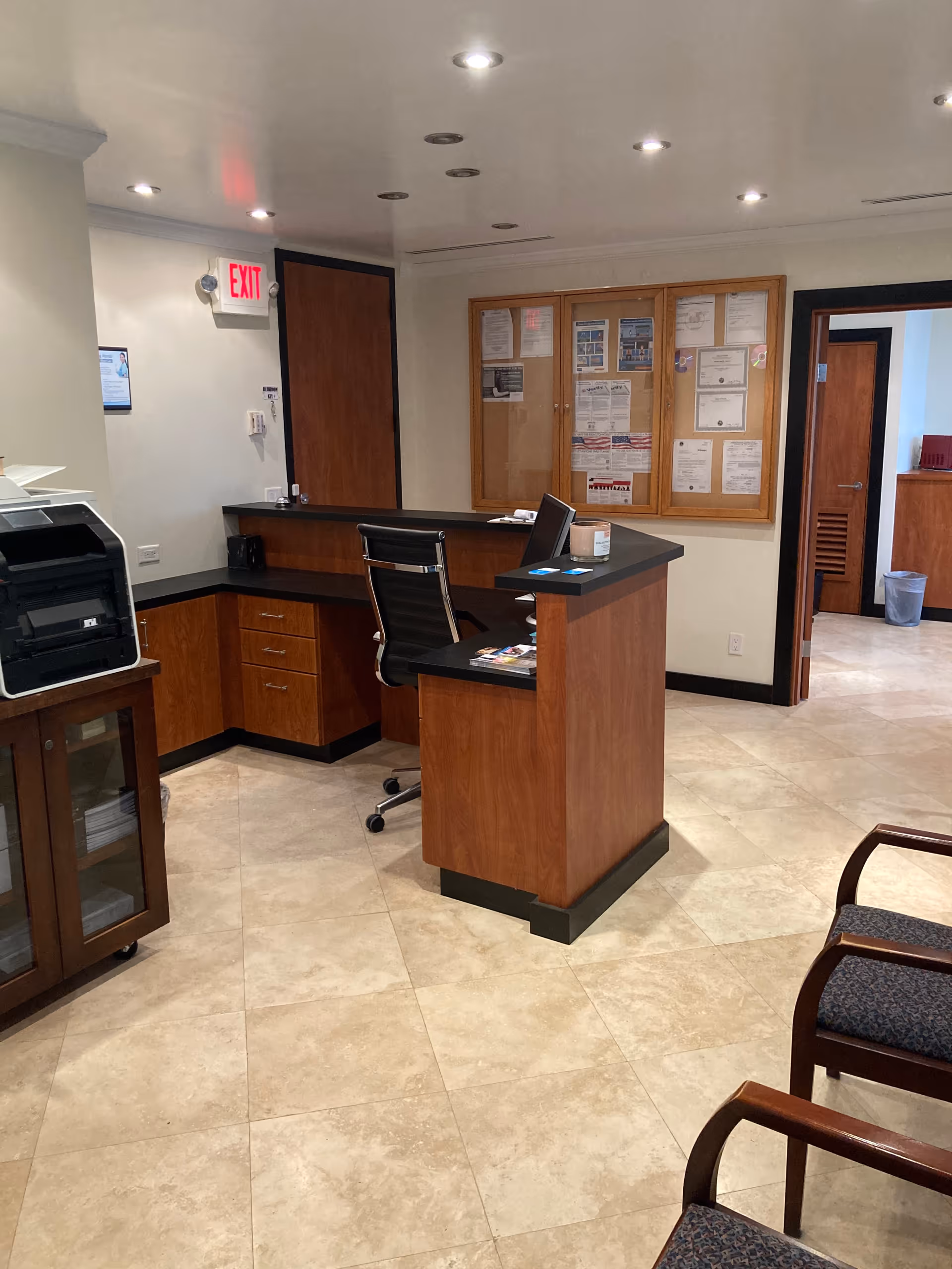 Reception desk in a well-lit lobby with bulletin board and seating.