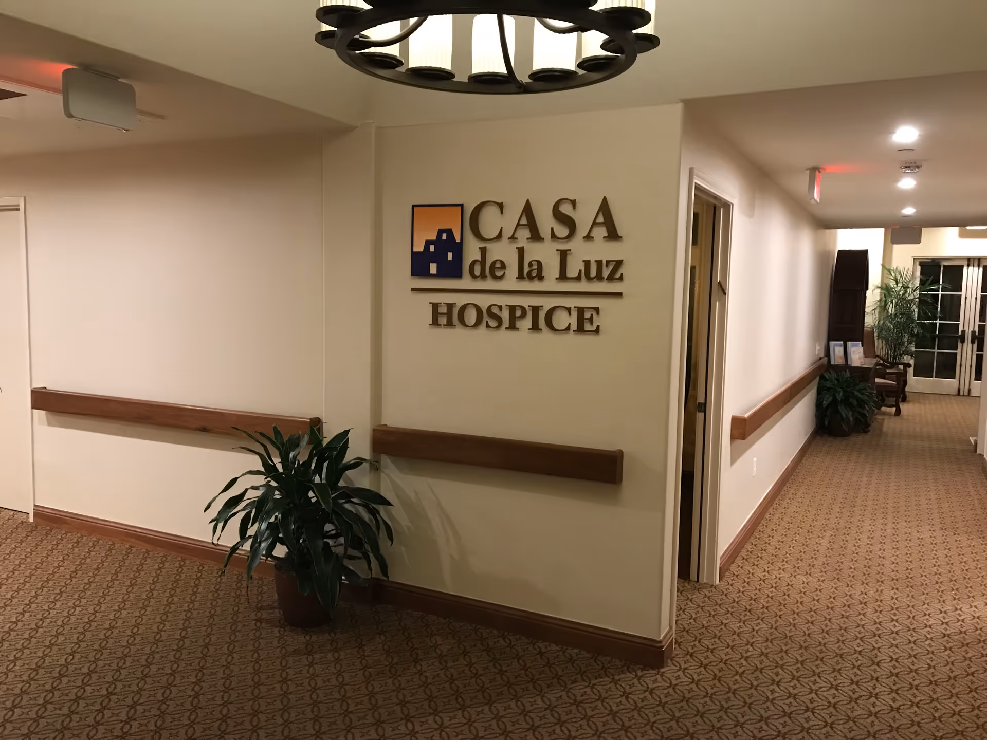Interior hallway at Casa de la Luz Hospice with sign and potted plants.