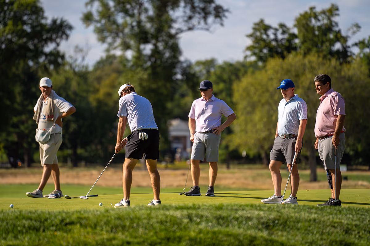 Group of older men on a golf course preparing to putt.
