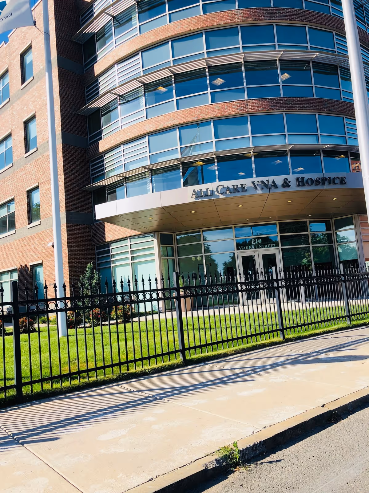 Exterior of All Care facility with curved glass windows and a black iron fence.