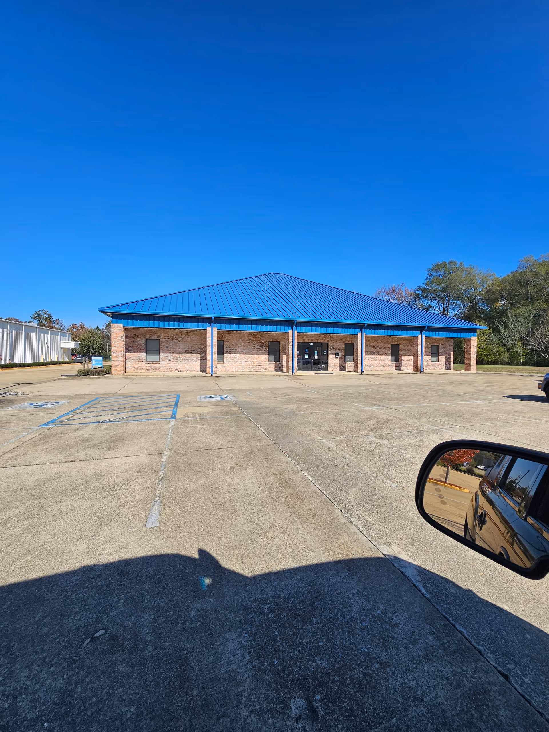 Front view of a brick facility with a blue roof and empty parking lot.
