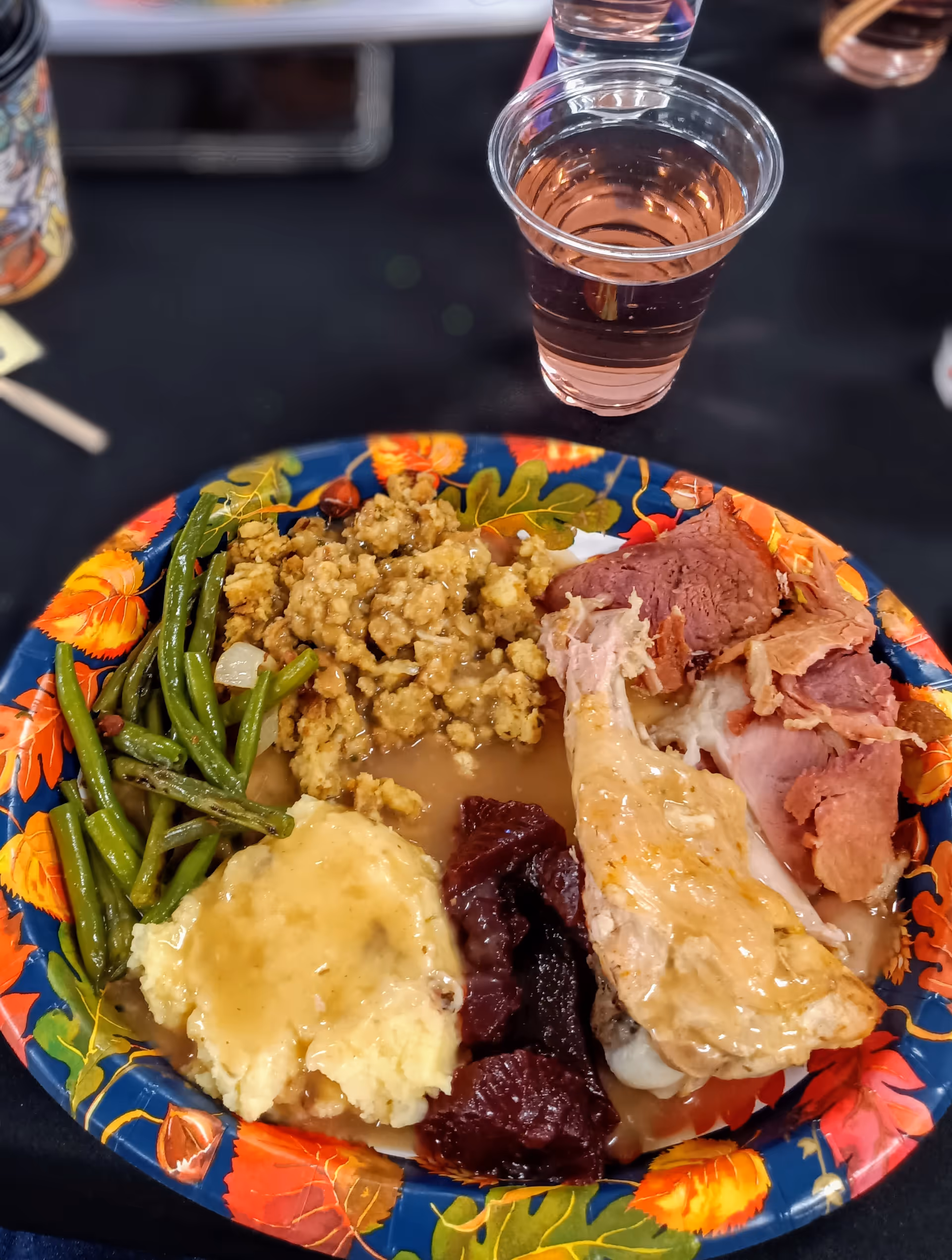 Colorful plate with turkey, stuffing, mashed potatoes, green beans, and cranberry sauce on a table.