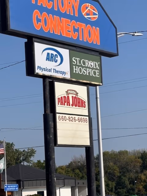 Tall outdoor signpost with St. Croix Hospice and other business signs against blue sky.