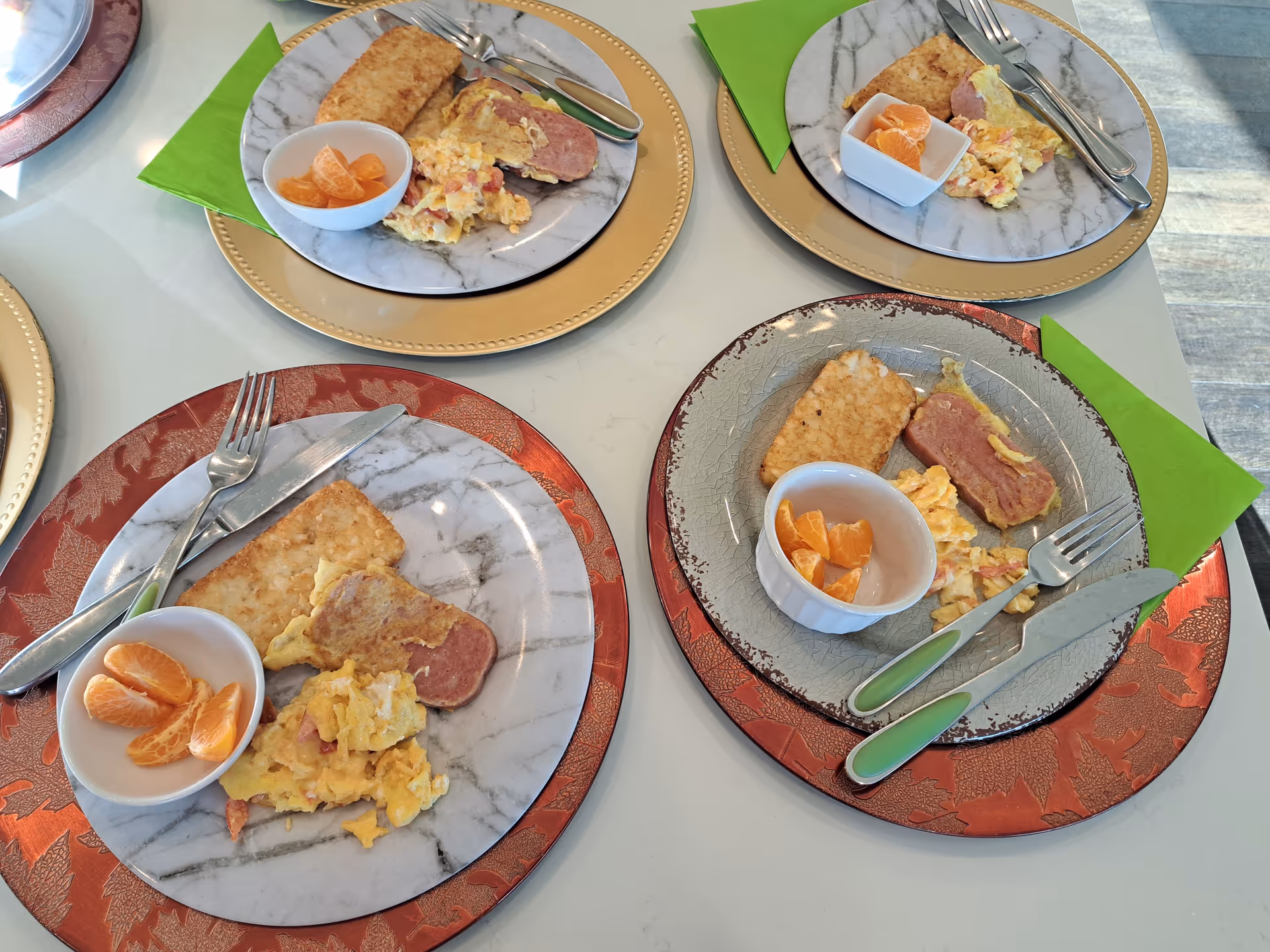 Top-down view of a dining table with plated meals, orange segments, and green napkins.