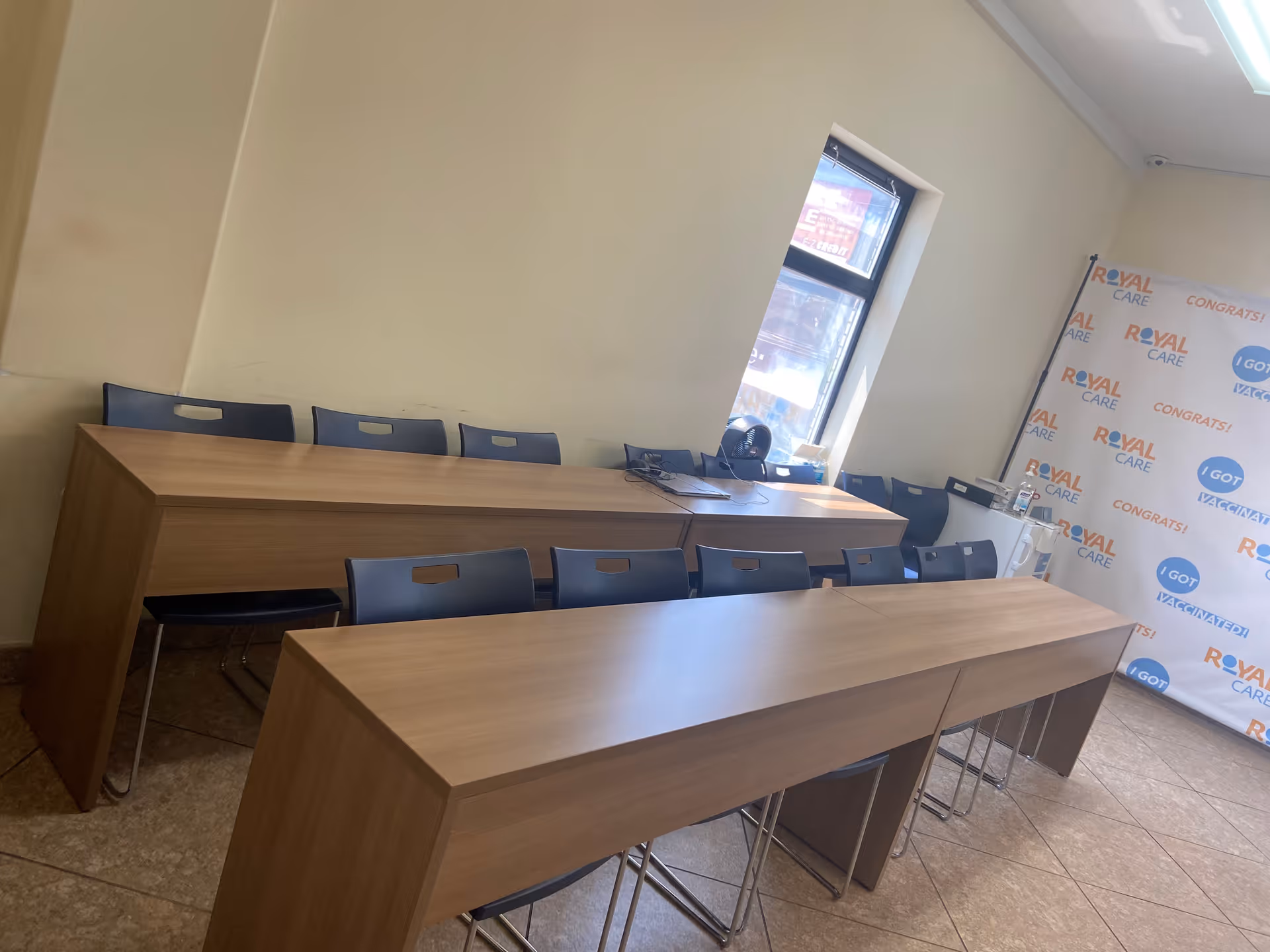 A conference room with long wooden desks, blue chairs, and a Royal Care backdrop.