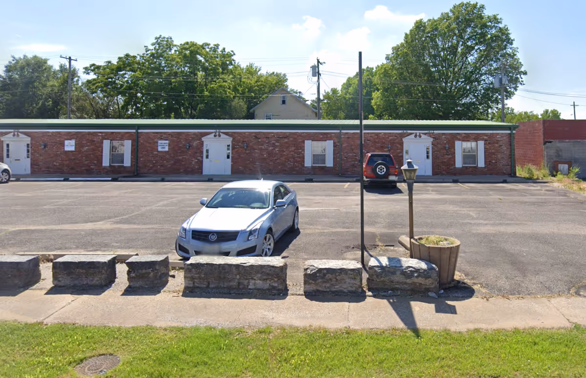 A brick, single-story building with a long facade and a parking lot in front.