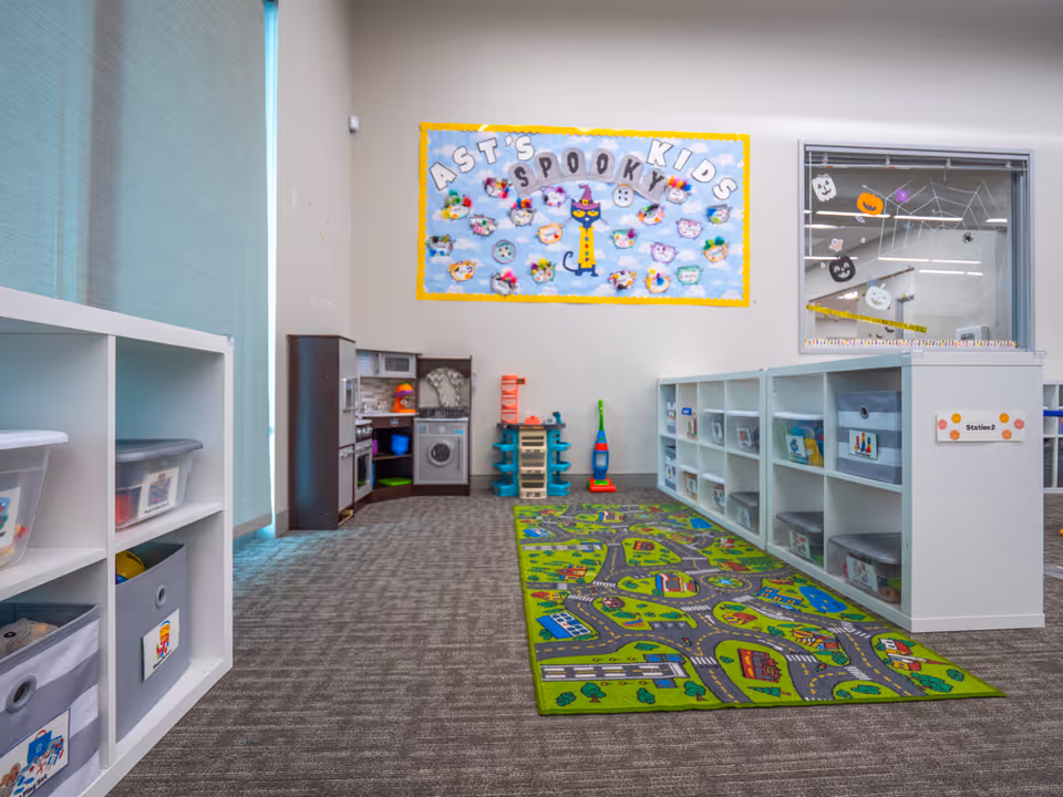 Indoor children's play area with colorful rug, cubbies, toy kitchen and play equipment.