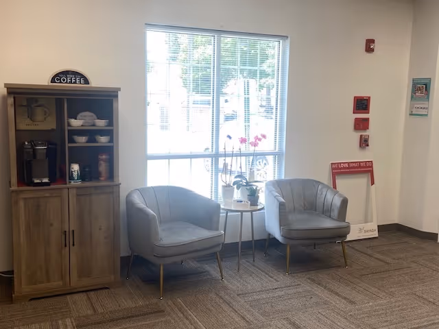 A cozy lounge area with two gray chairs, a coffee station, and plants.